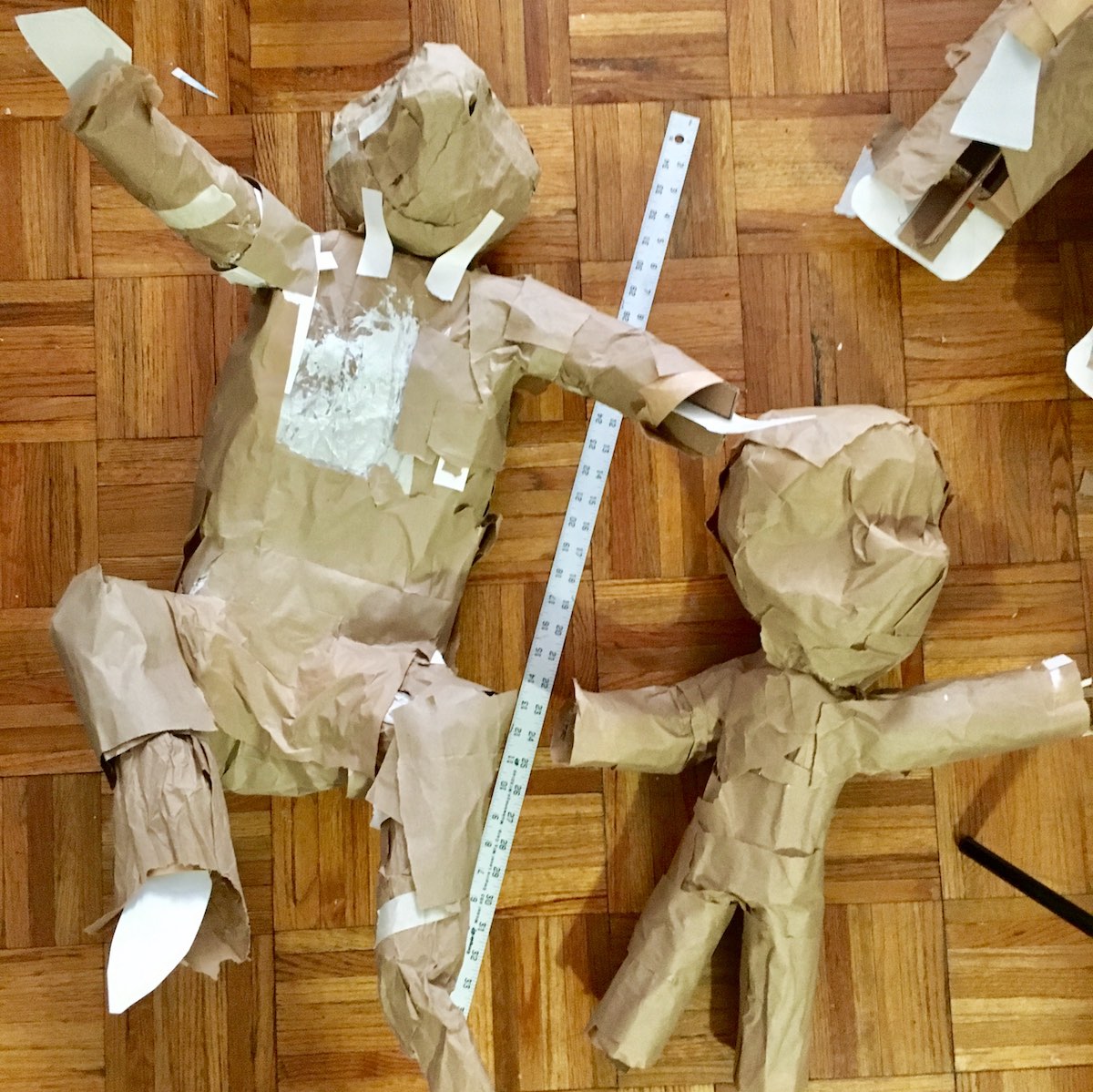 Posed armatures of a crouching lemur and a waving Bobby, wrapped in brown paper