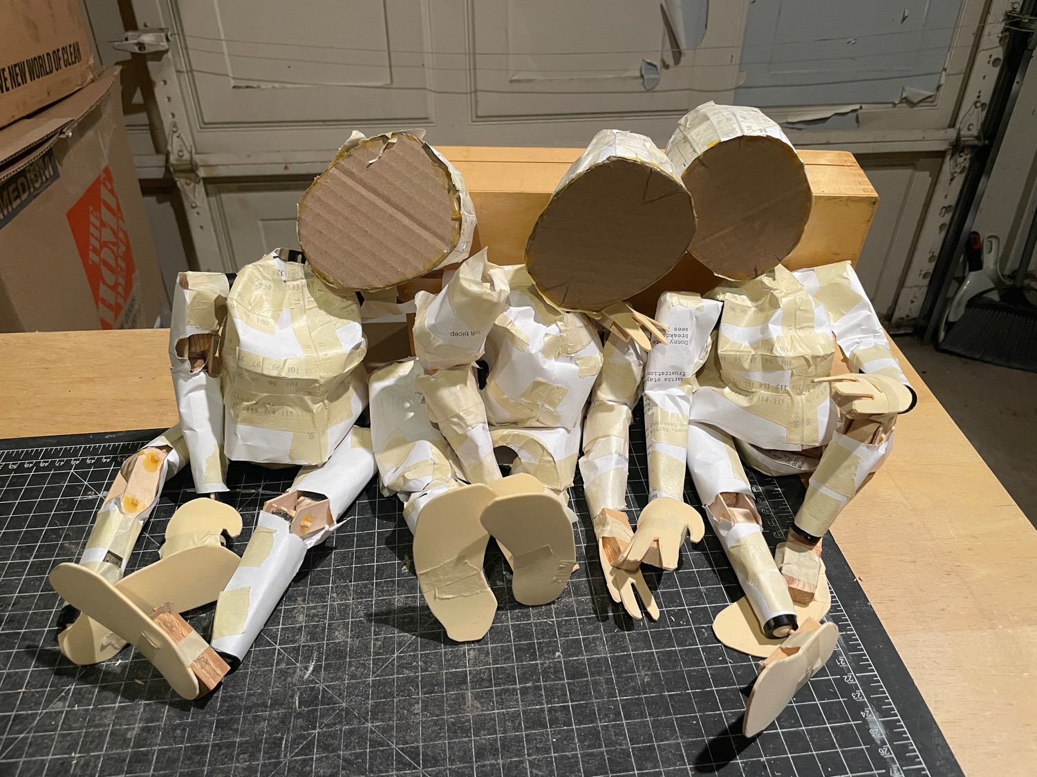 Three humanoid characters made of wood and paper and cardboard and foam, sitting together in a friendly way