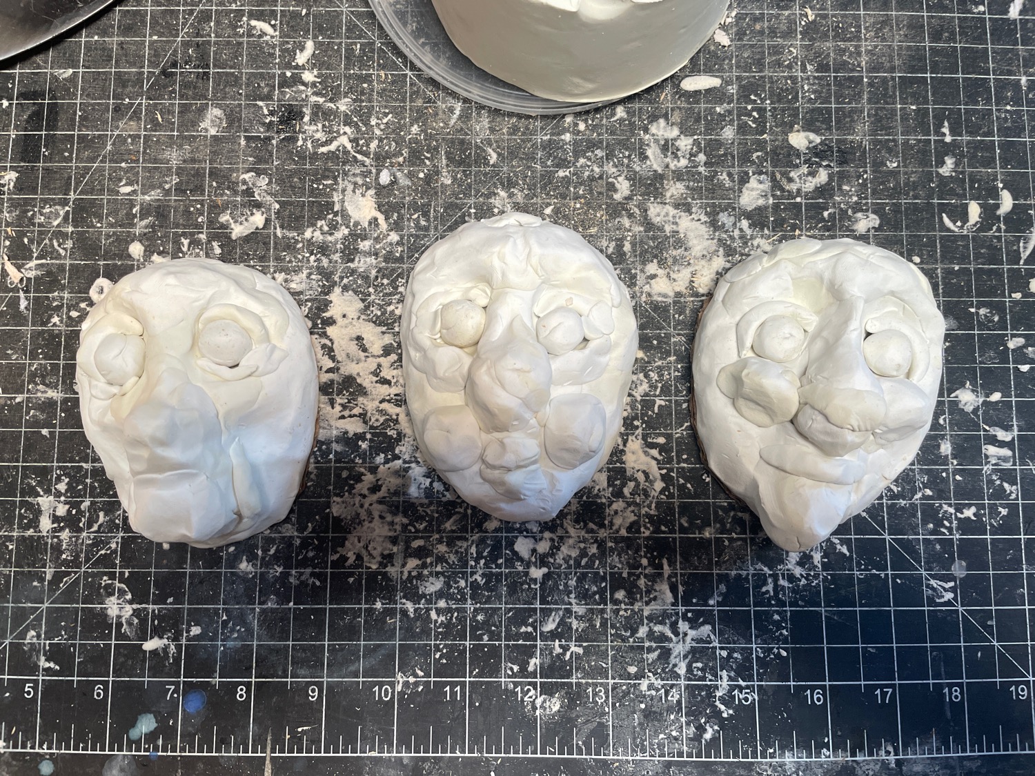 Three blobby faces made of rough bits of clay, laid out on a very dirty cutting mat
