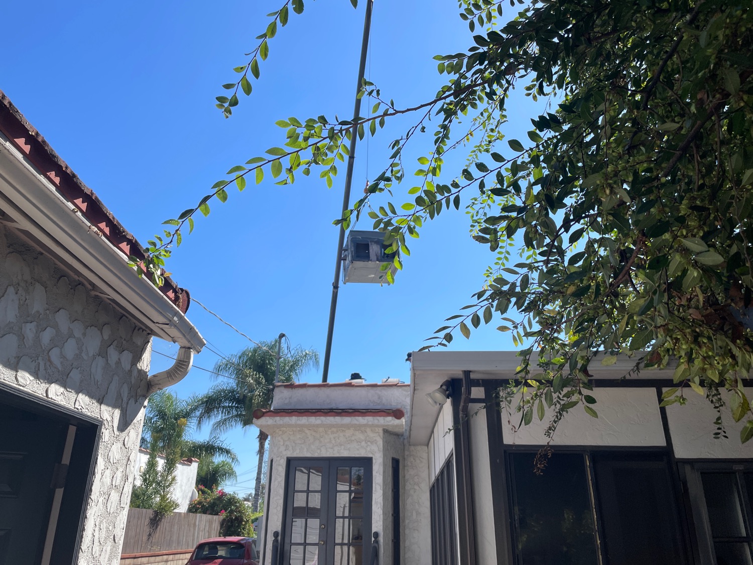 A crane lifting a huge metal box up into the sky above the house