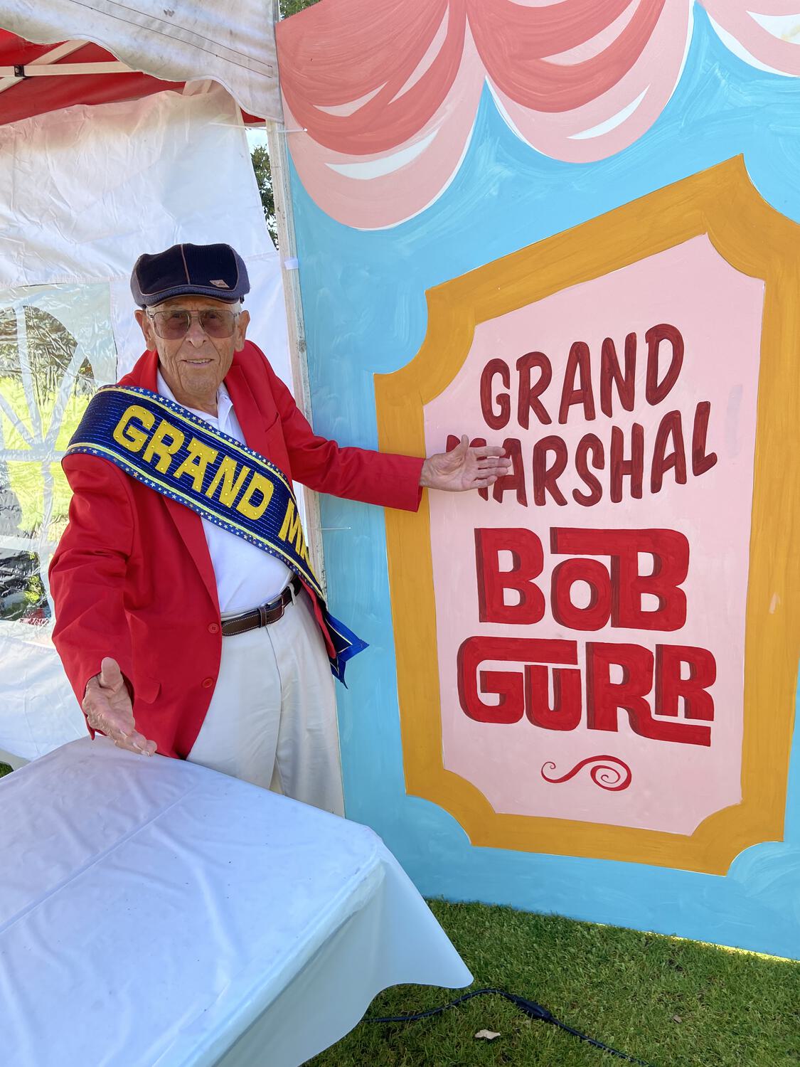 Bob Gurr posing in front of a sign that reads "Grand Marshal Bob Gurr"