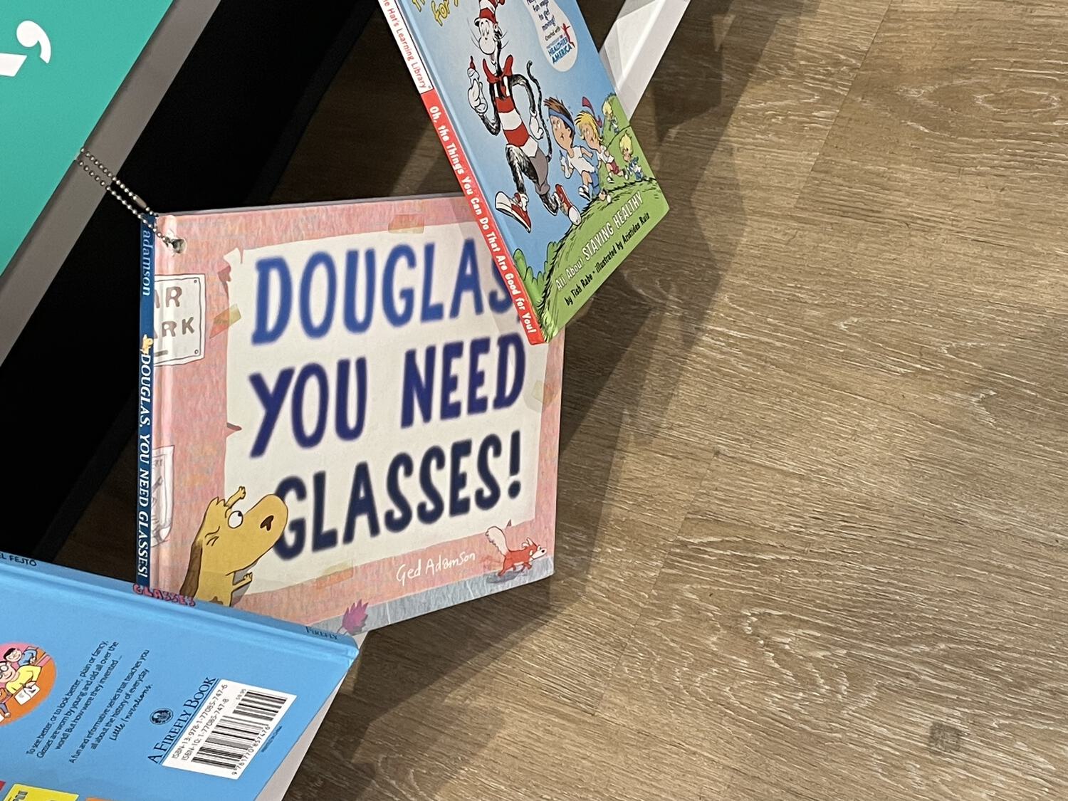 A book hanging by a chain from a counter. Its title is "Douglas, You Need Glasses!"