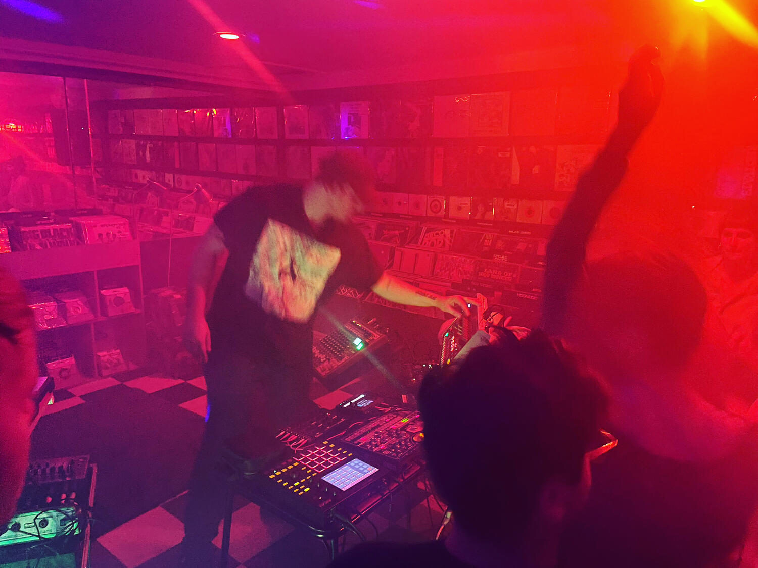 An electronic musician tweaking a synth under multicolored lights in front of a crowd