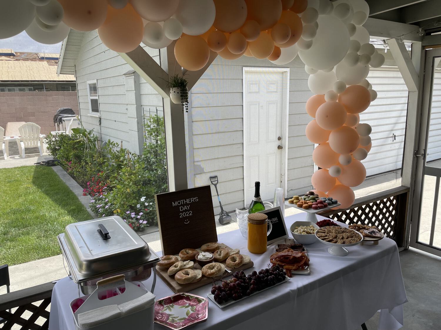 Lots of brunch food spread out on a table with decorations and a sign that reads "Mother's Day 2022"
