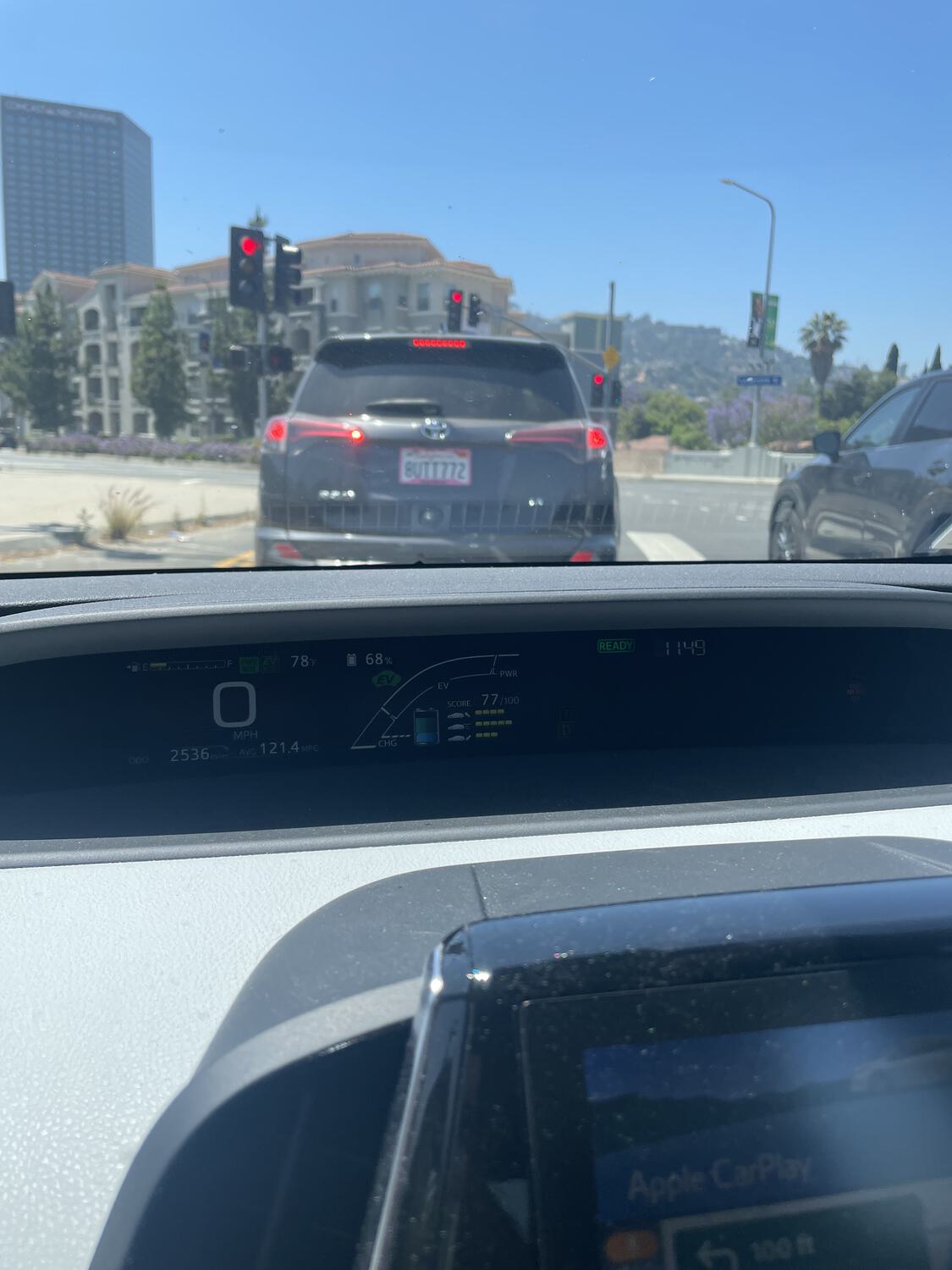 A photo taken discreetly from the driver's side, over the dashboard, of a car stopped at a red light. Its license plate reads BUTT772