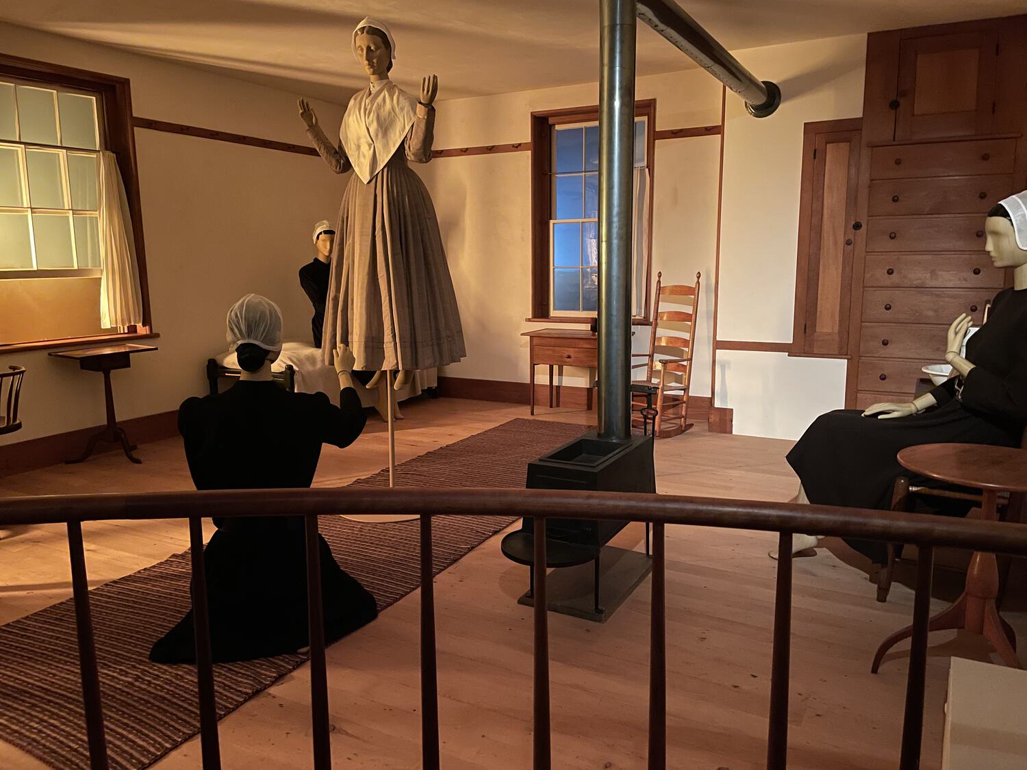 Mannequins dressed like Quakers are scattered around a period room. One is floating a few feet above the ground while another kneels before her.