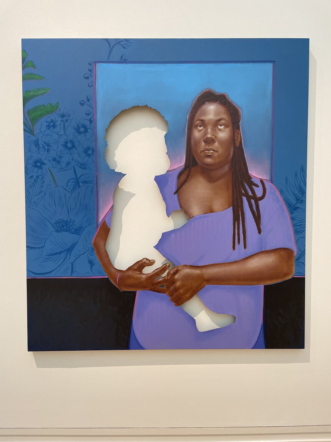 A painting of a Black woman holding a baby in her arms and looking up to the sky. The baby has been cut out of the canvas, leaving a white silhouette of the wall in its place.