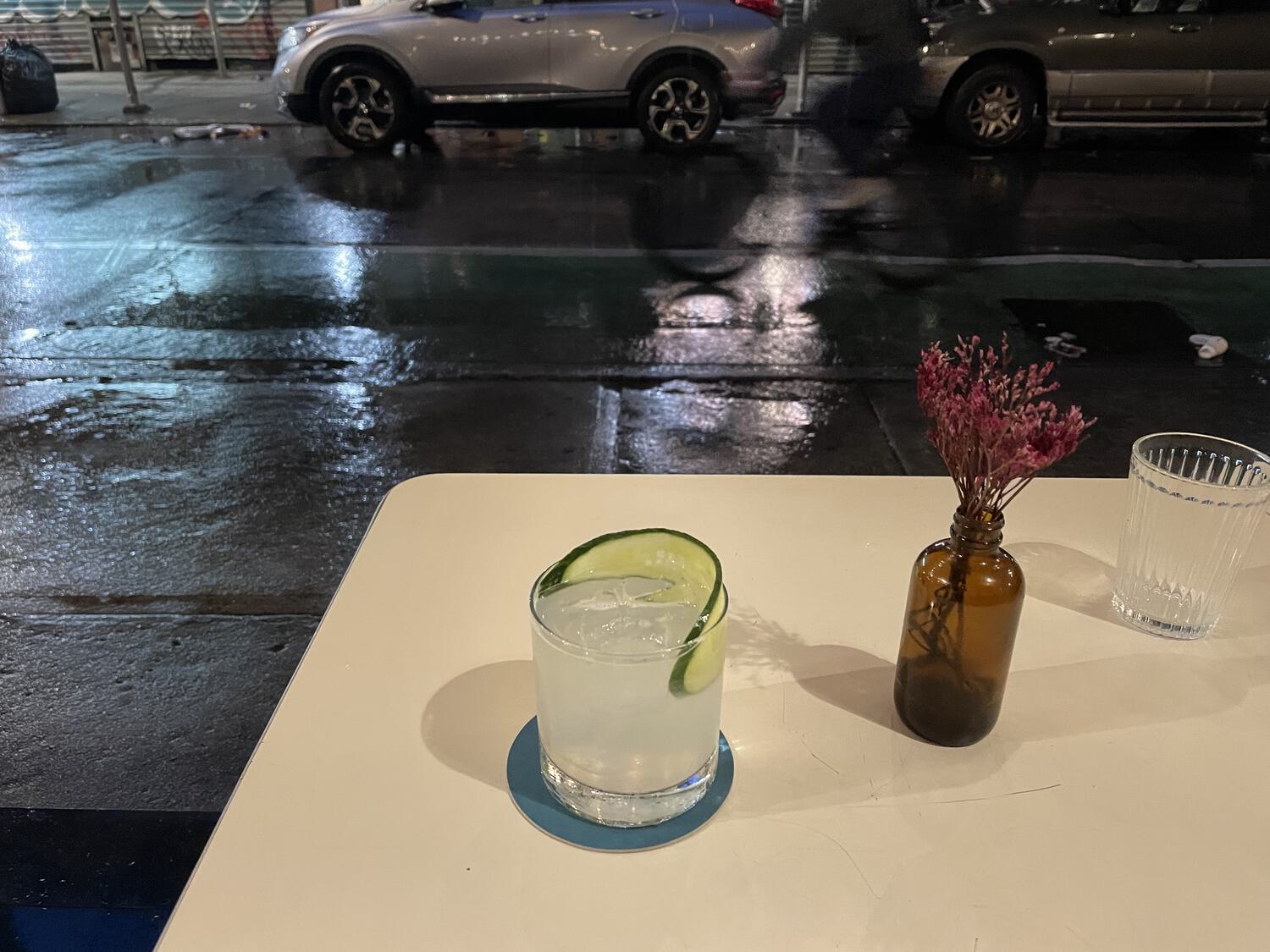 A cocktail and table setting on a table outdoors with a very wet street behind it