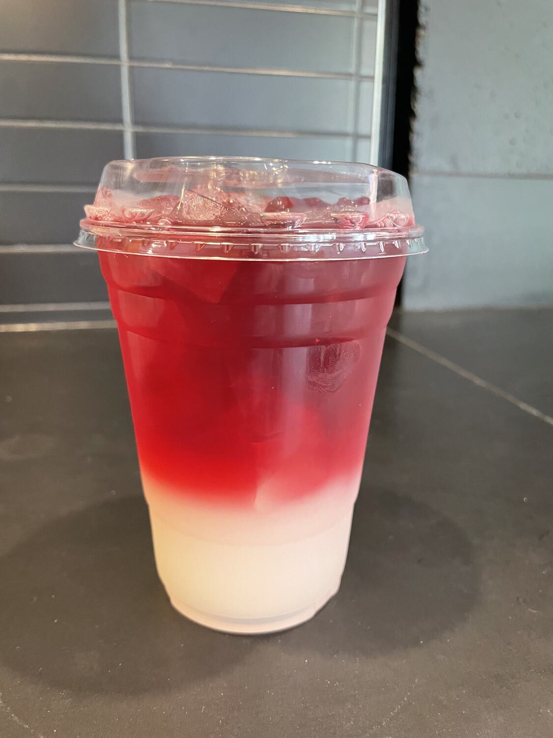 An iced drink in a disposable cup; the top two-thirds are a deep red and the rest is a pale yellow