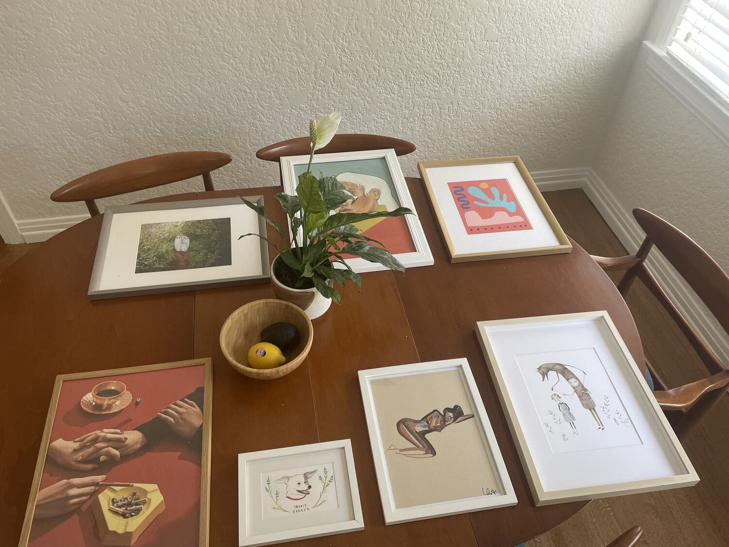 Framed prints and photographs arranged on the dining table in the way they'll be mounted on the wall