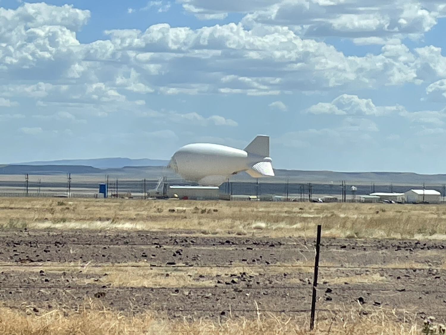 A distant blimp in the desert, tethered to the ground