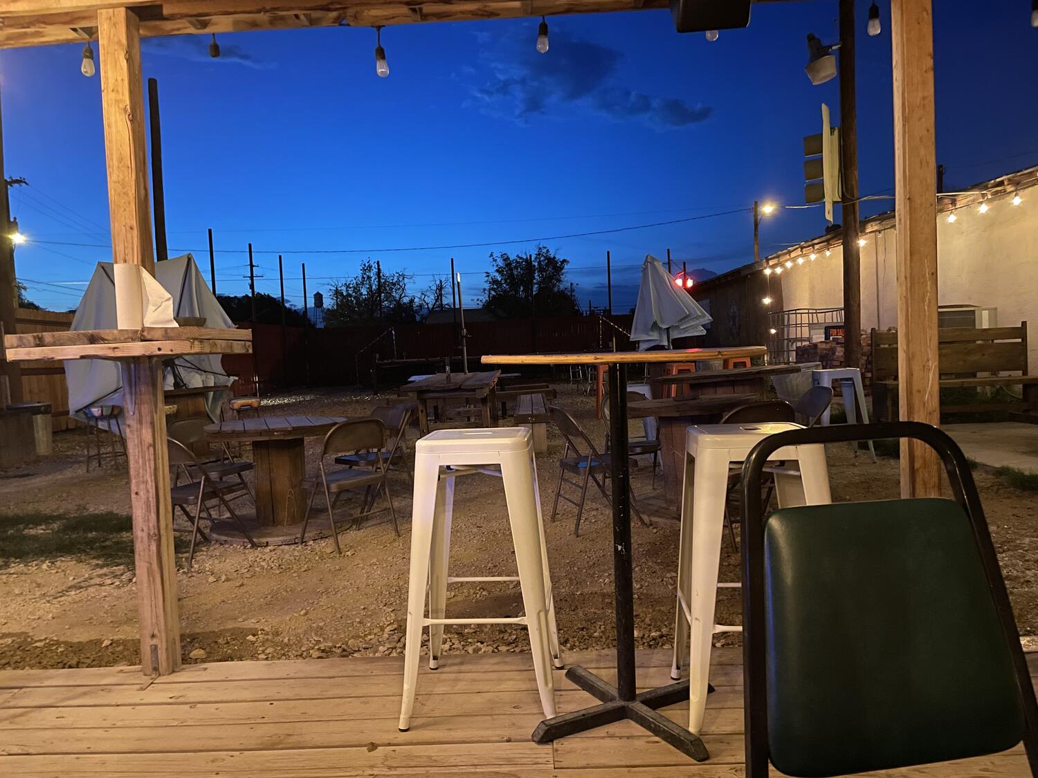 A rough wooden porch overlooking a dirt yard full of mismatched chairs and tables