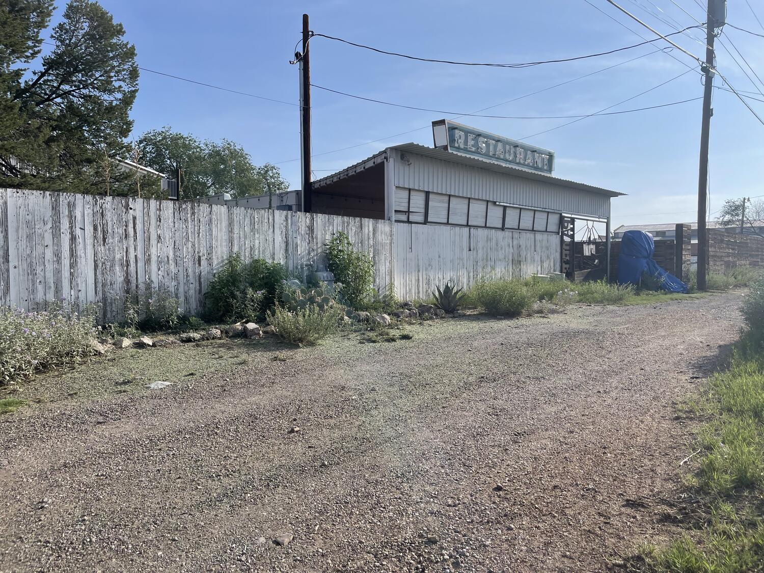 A gravel road, an old wood fence, and an interesting-looking building with a big neon sign that reads RESTAURANT. Looks like it's maybe from the 50s and maybe hasn't been open since then.