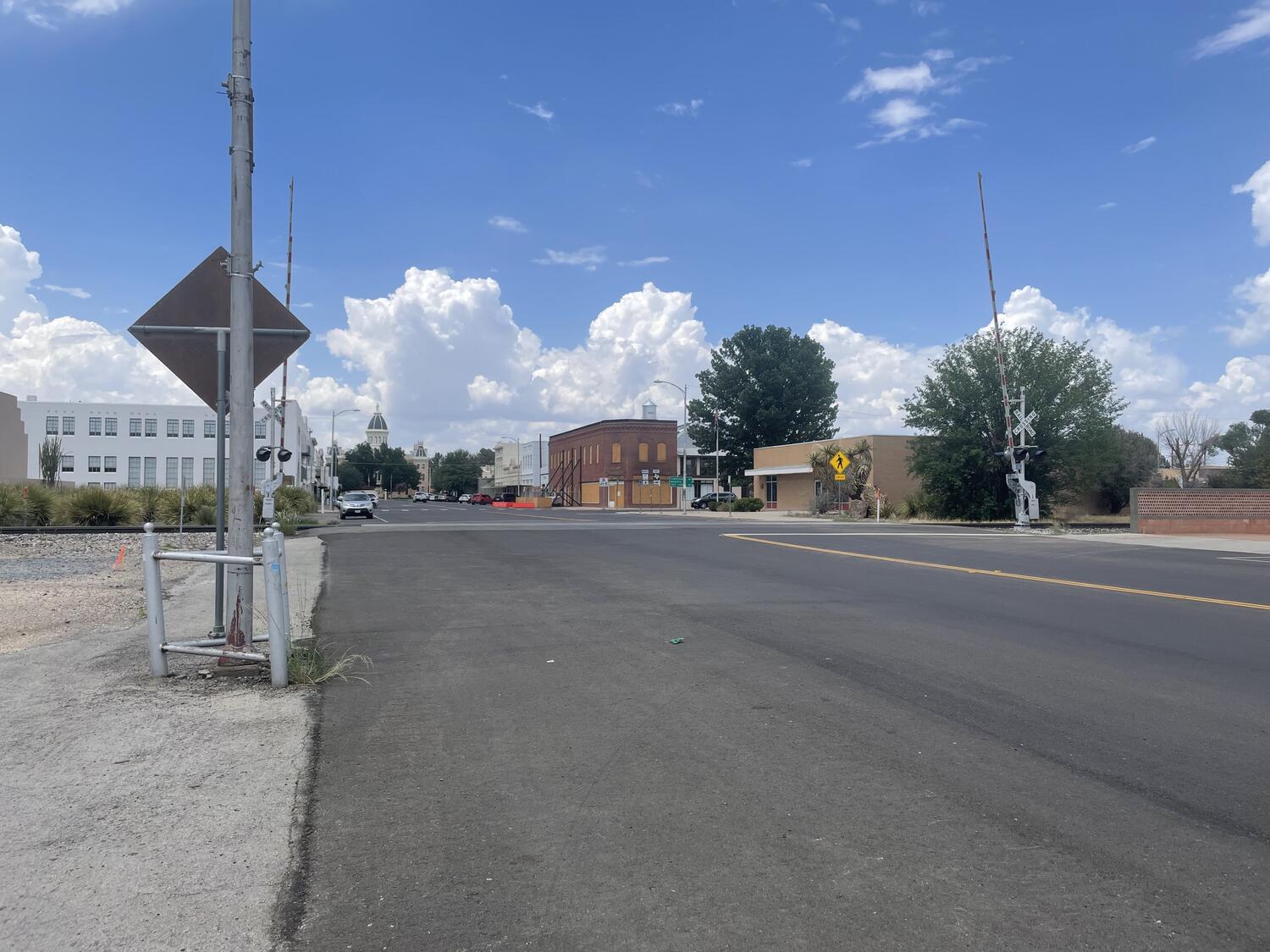 A quiet intersection in Marfa. Wide empty streets, a railroad crossing, and City Hall in the far distance. Big sky, puffy clouds.