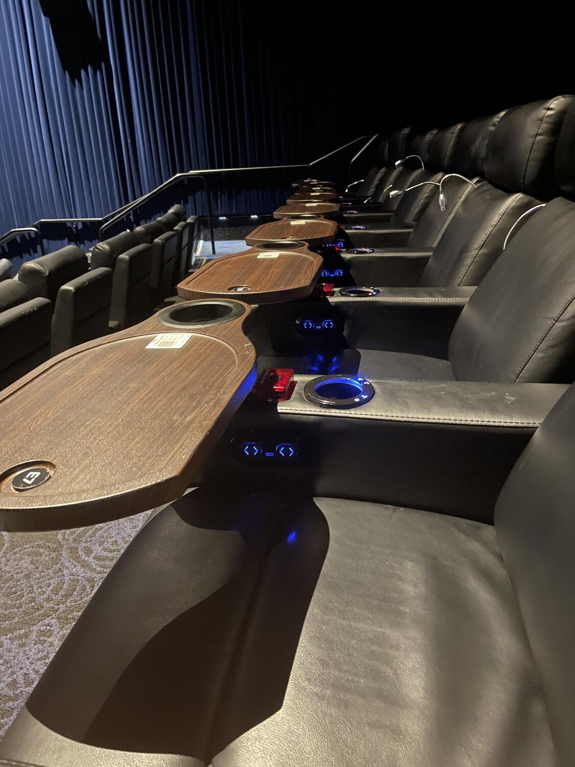 Plush seats with built-in tables in a movie theater. The house lights are still up and there's no one here.