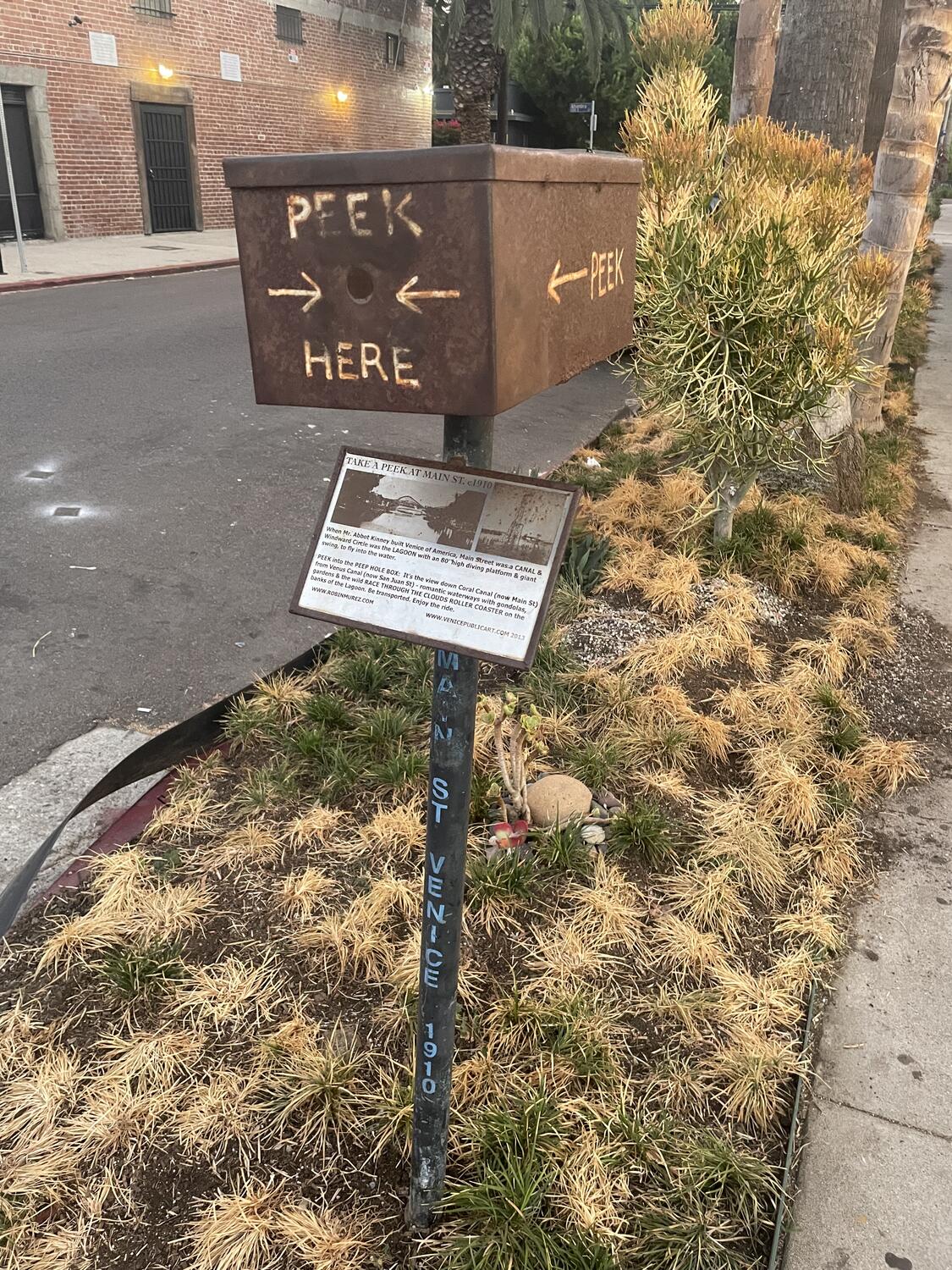 A rusty wooden box on a pole, about the size of a shoebox and at roughly head-height. There's a whole punched in one side and it says PEEK HERE