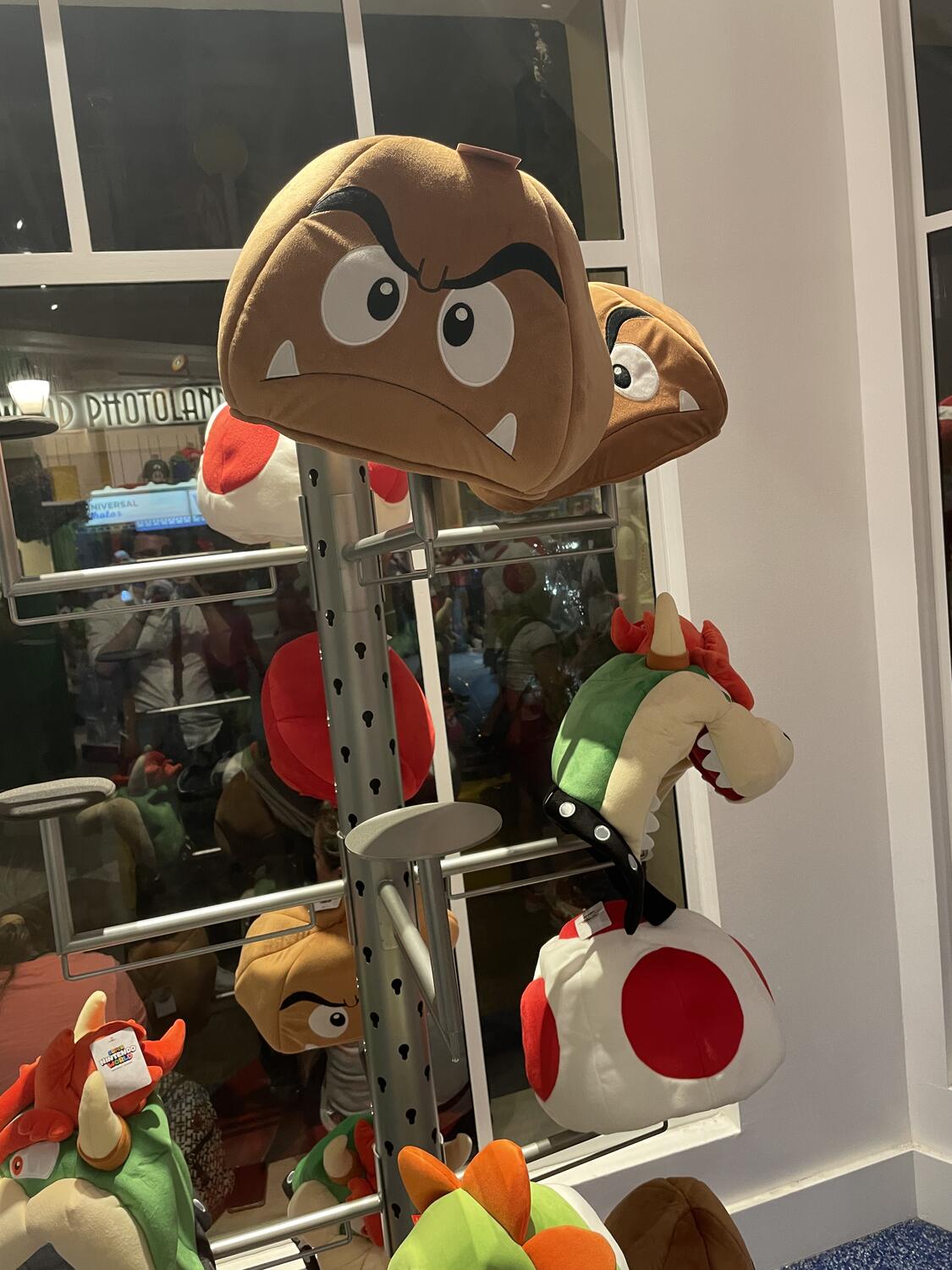 A hat stand in a gift shop. Lots of Mario characters made to be oversized hats—goombas, Bowser, and Toad