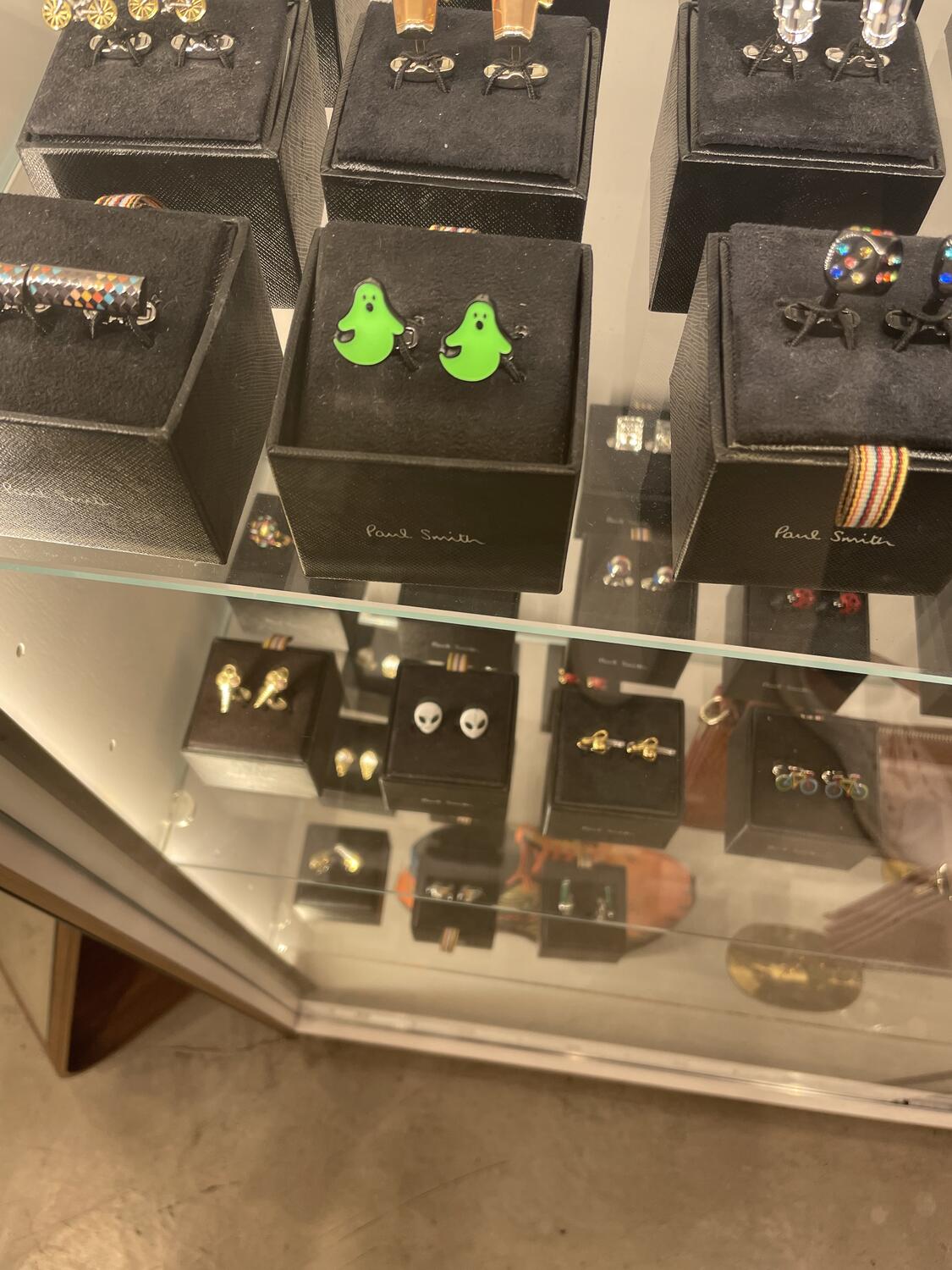 A display case full of novelty cuff links. In the center are glow-in-the-dark green ghosts, but we can also see aliens, bicycles, colorful dice, and more.