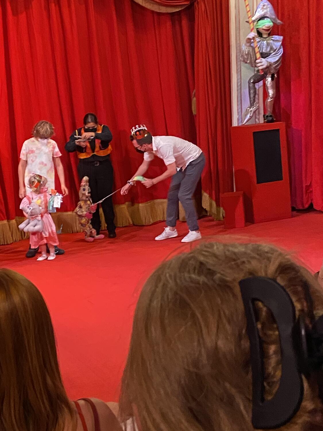 Me up on stage! I'm leaning over to pull a little gift bag from the hand of a dog marionette. I have a paper crown on my head. A small child is beside me, doing the same thing.