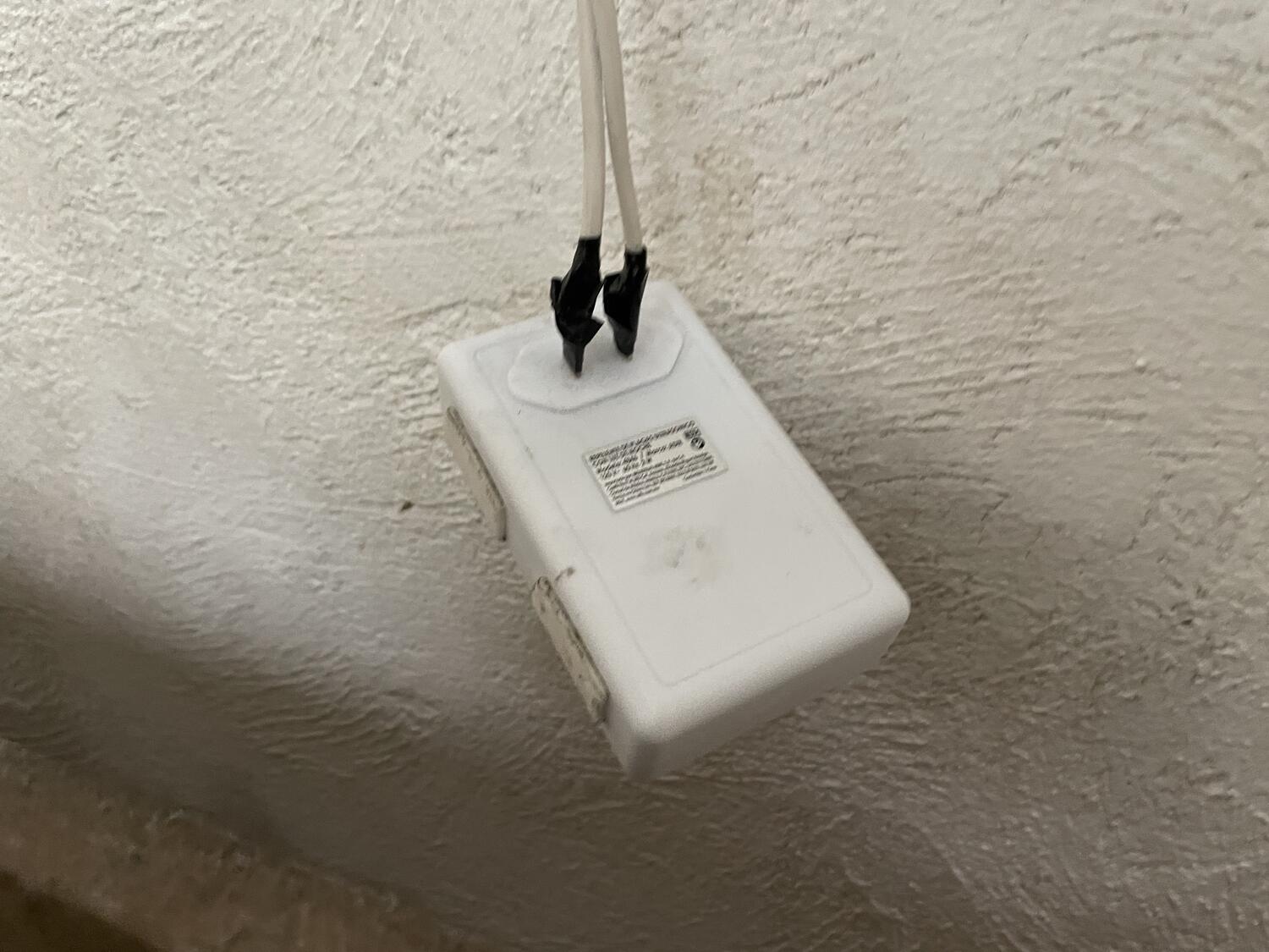 A power cord whose bare wires are attached to the prongs of some kind of appliance, maybe a carbon monoxide detector with electrical tape. It's just hanging in the air against the wall, suspended by the cord, which continue up and out of frame