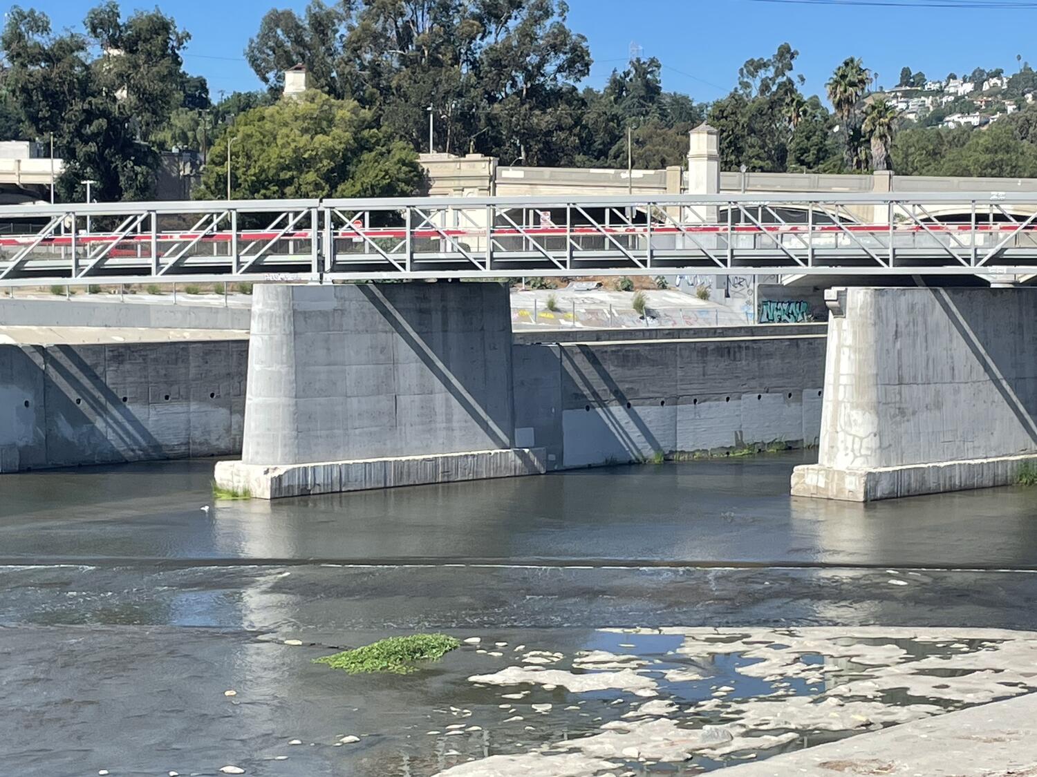 The Red Car foot bridge over the LA River, seen from a distance. It's a spare metal bridge with a red handrail running the whole length.