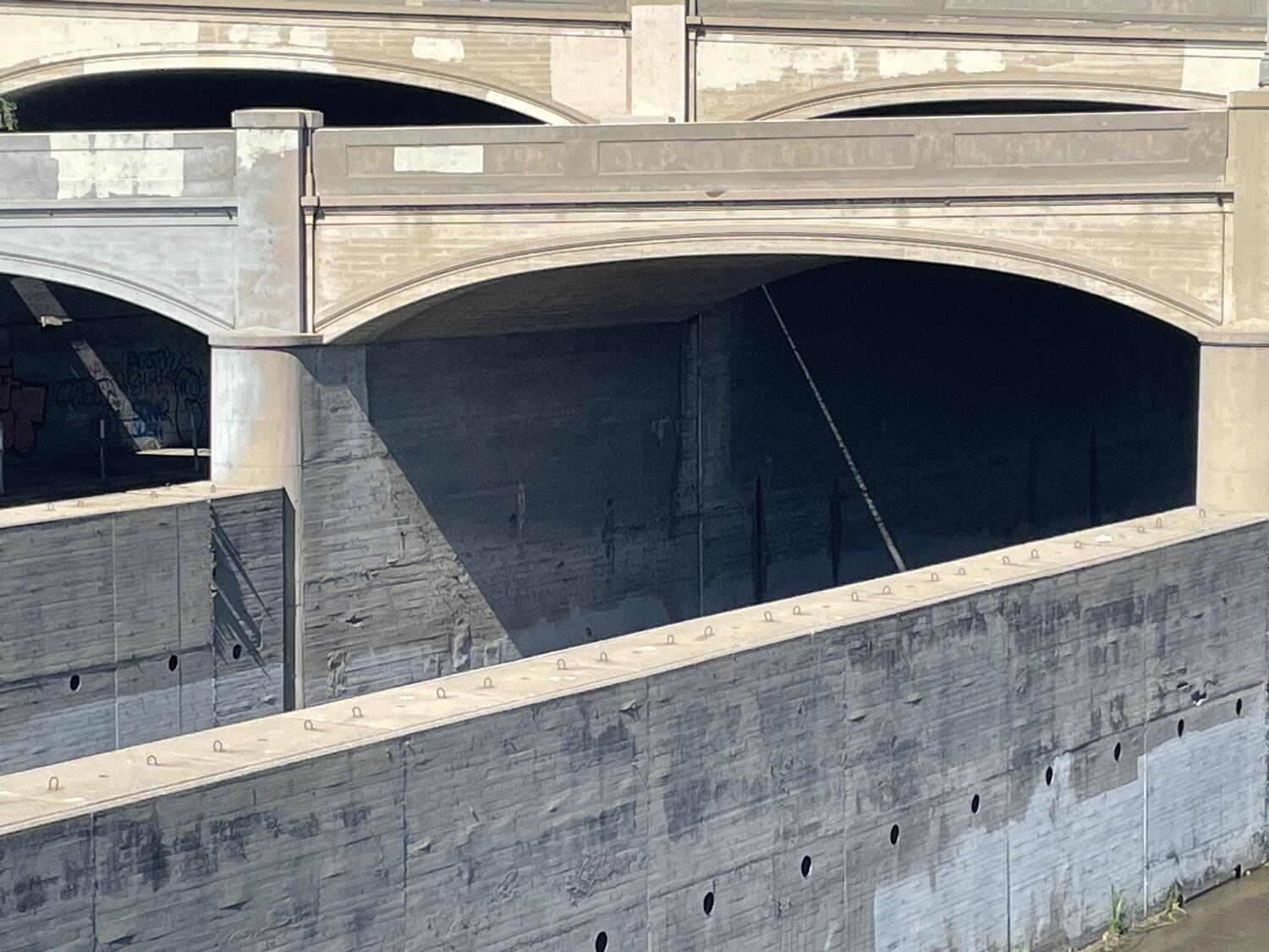 A distant shot of some architectural detail on a bridge across the LA river. Various horizontal arches and perpendicular supporting walls meet at unexpected angles, creating interesting shadows and lines of sight.