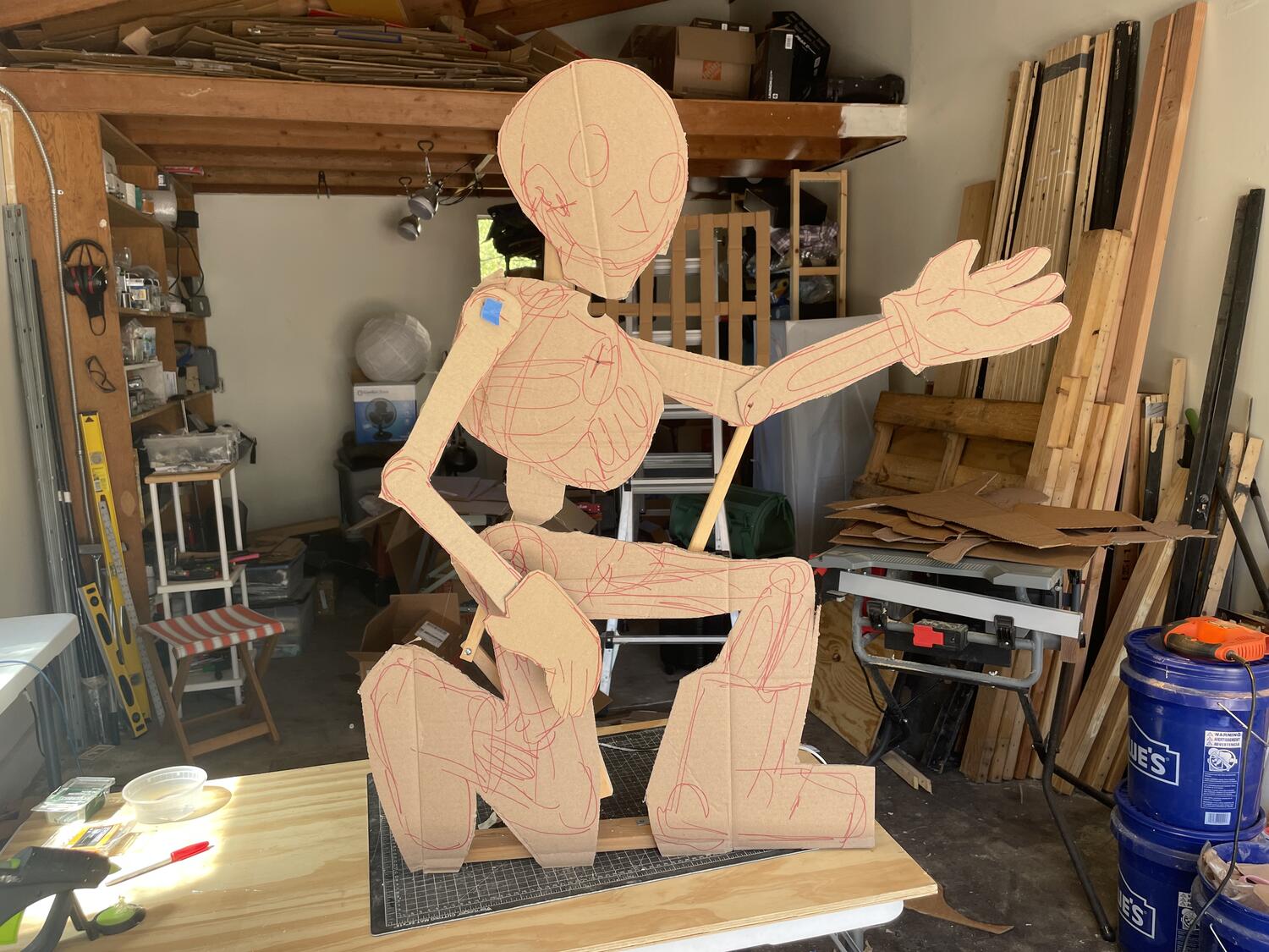 A skeleton sculpture made of cardboard. It's kneeling with an outstretched hand, and there's a wooden armature barely visible behind it that apparently enables movement