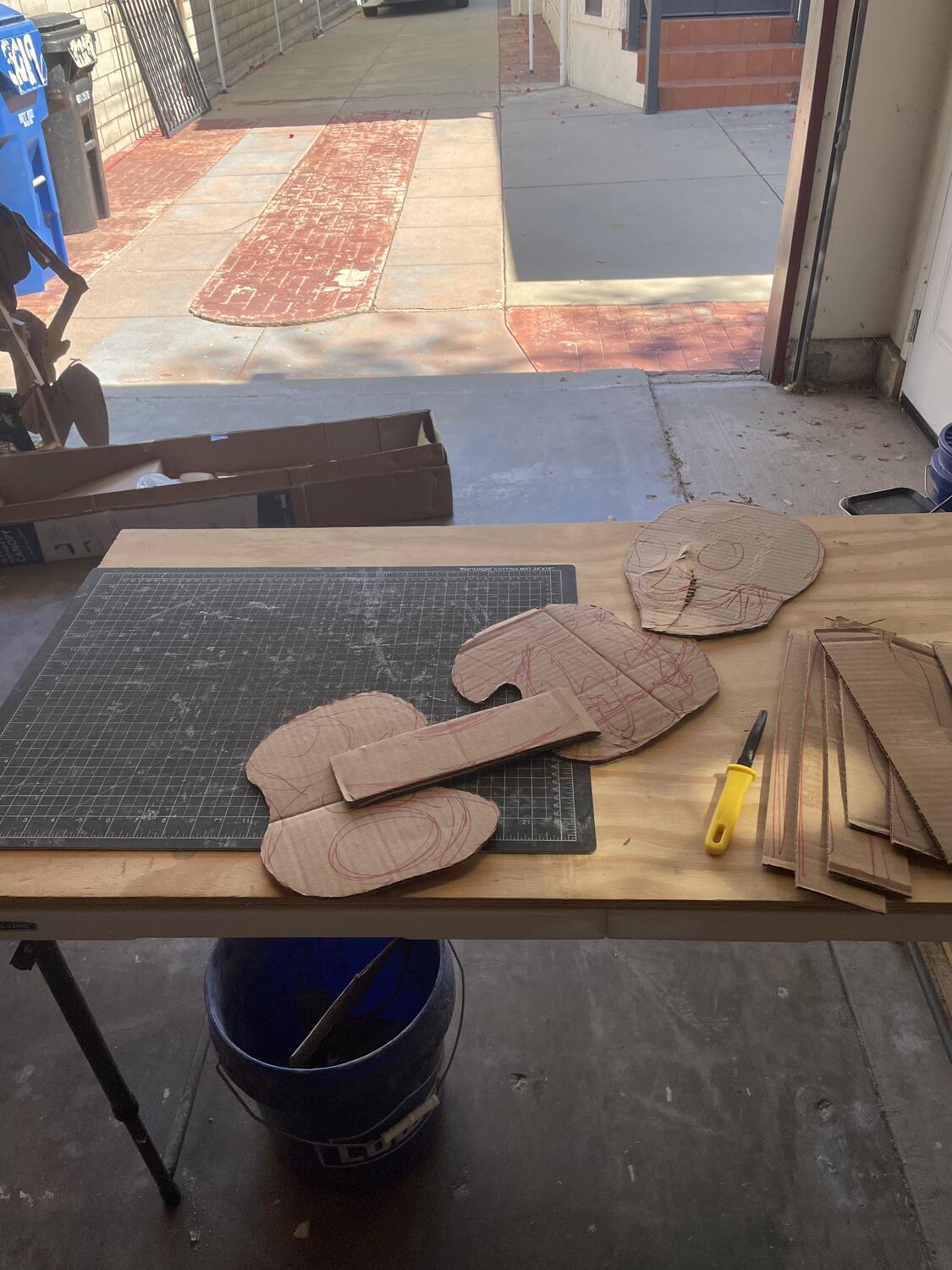 Some cardboard shapes laid out on the table forming a head, ribcage, and hips for a skeleton. More strips of cardboard are ready to be included, and a small black knife with a yellow plastic handle sits among it all.