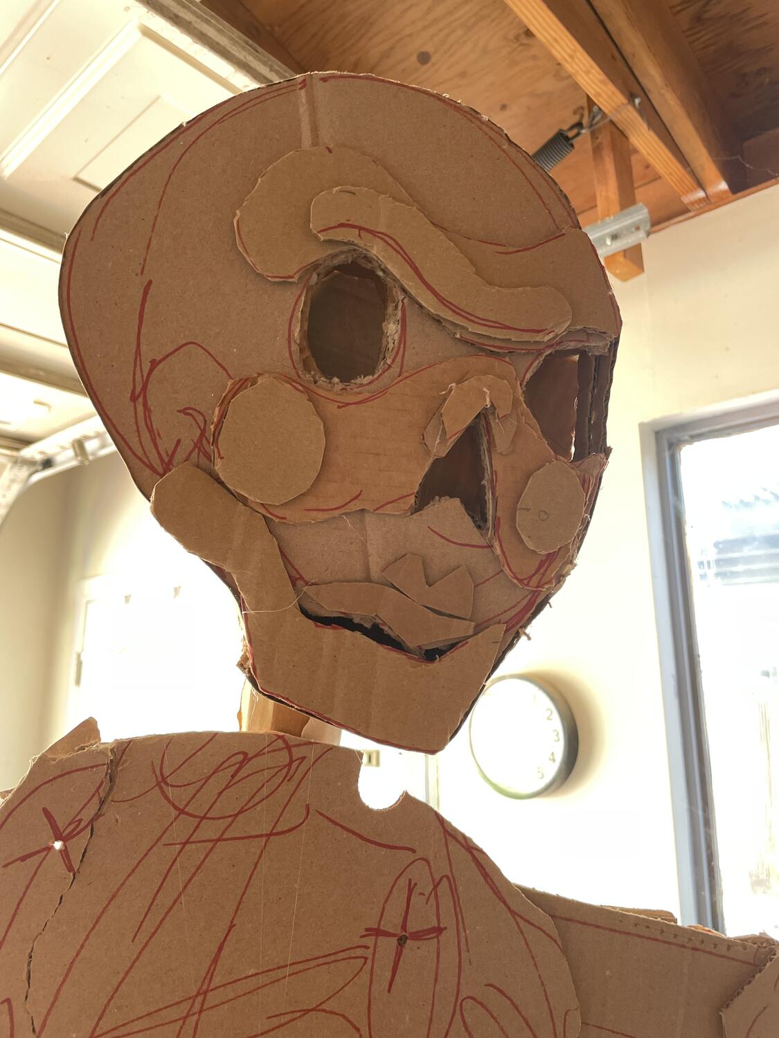 A cardboard sculpture. It's a skeleton with an exaggerated expression. The piece is mostly flat, but layers of smaller shapes of cardboard give it a topographic depth