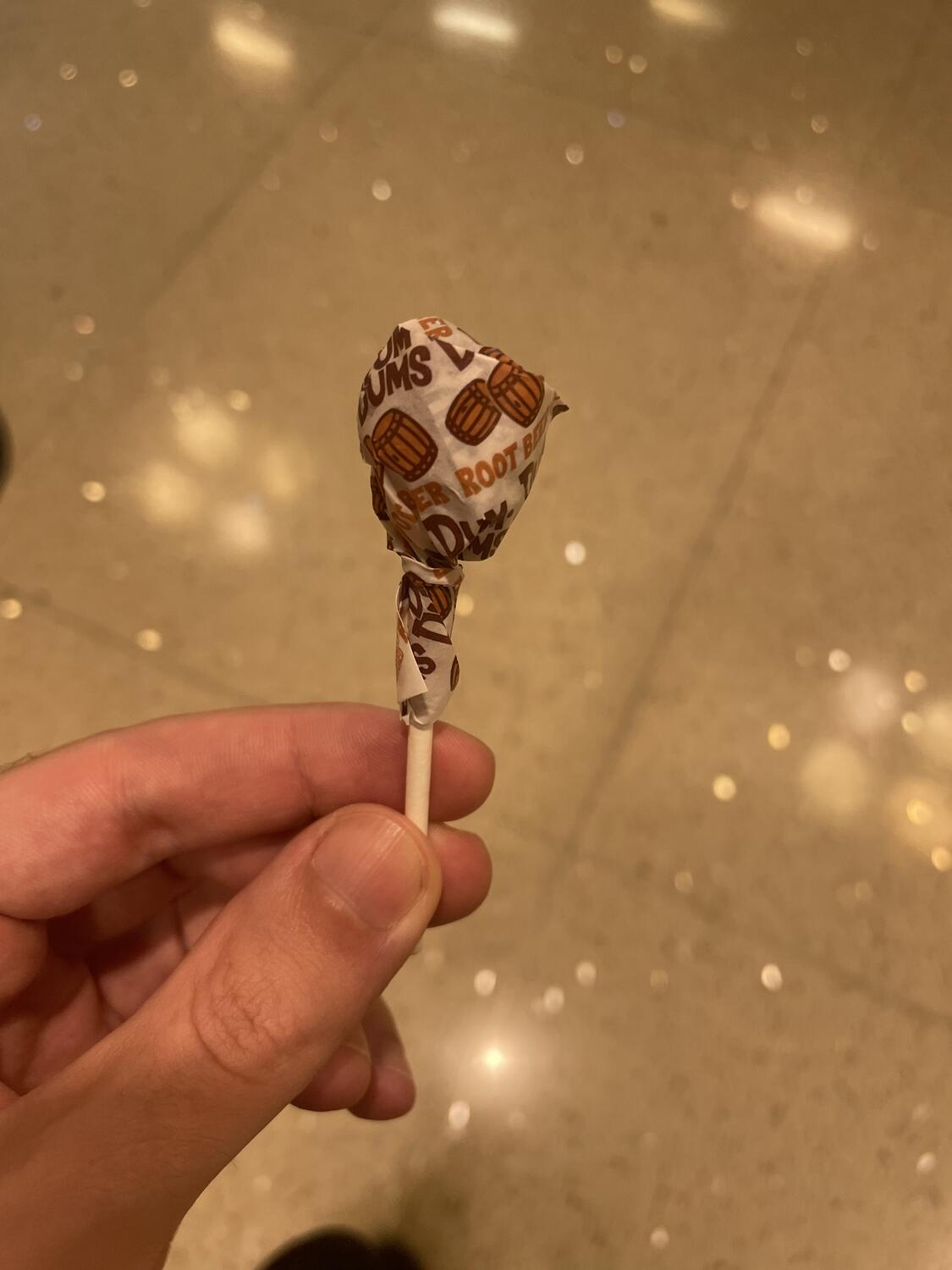 Holding a root beer Dum Dum Pop over a very clean tiled floor