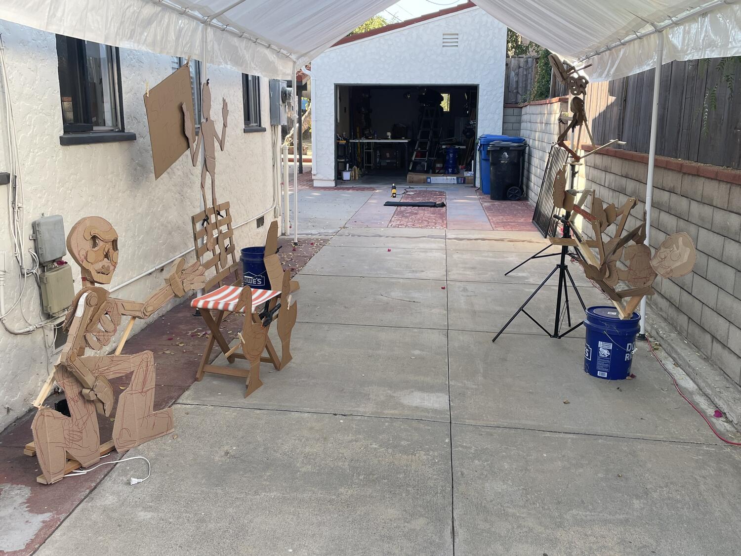 A head-on view down through the carport tent. Unpainted cardboard sculptures line the sides of the space, mostly filling out its length.