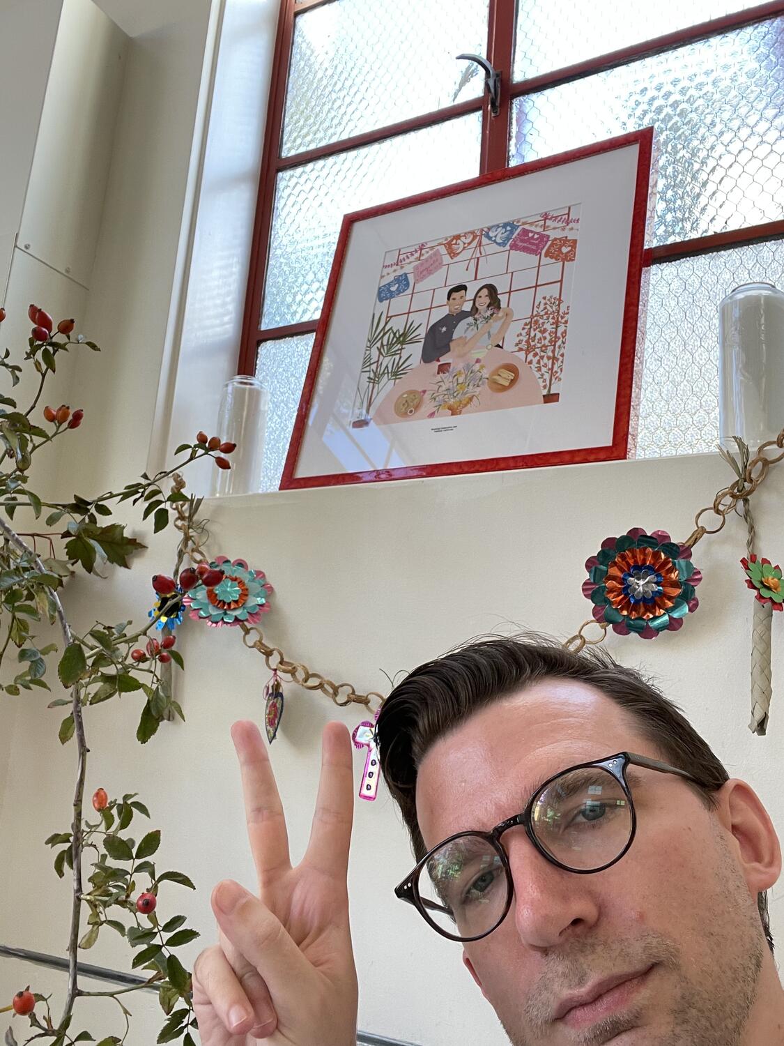 A selfie. I'm giving the peace sign, and behind me are some wedding decorations and a framed illustration of Zack and Ashley