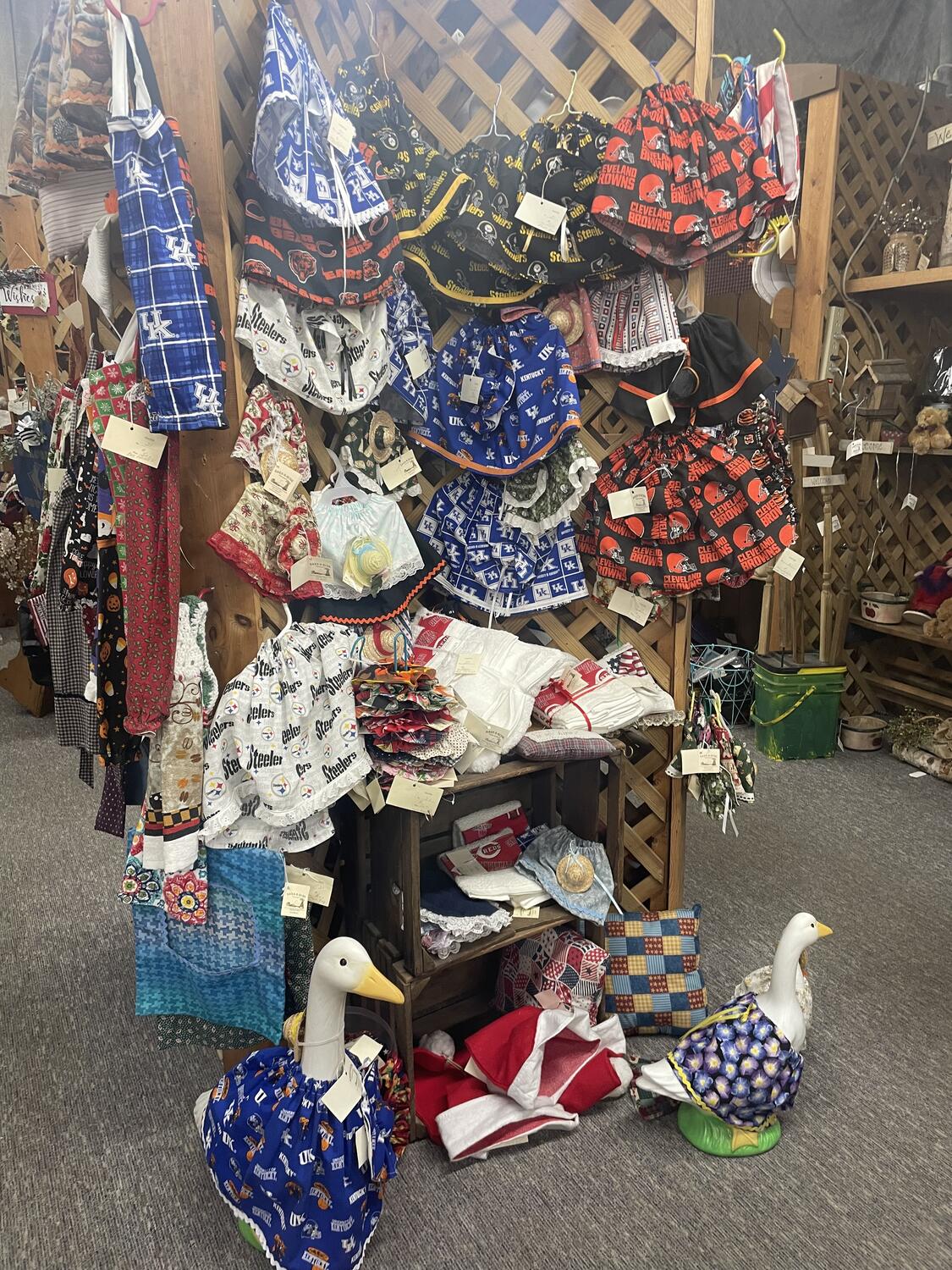 A handmade display of frocks that seem to be designed for duck statues—there are two ducks modeling them on the floor in front of the display