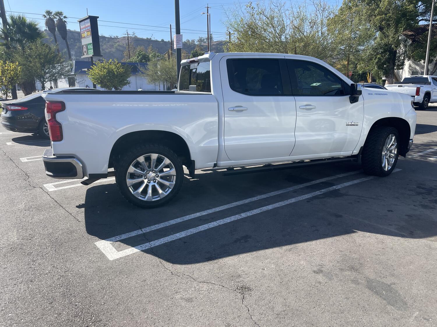 A huge white pickup truck parked diagonally across two spots in a parking lot