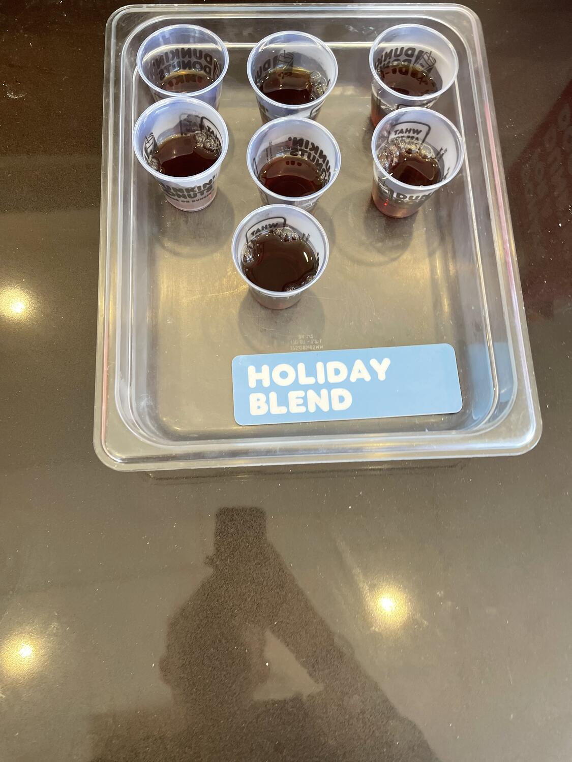 Small plastic cups half-filled with coffee, sitting in a plastic tray on the counter. A sign beside them reads â€œHoliday Blend.â€�