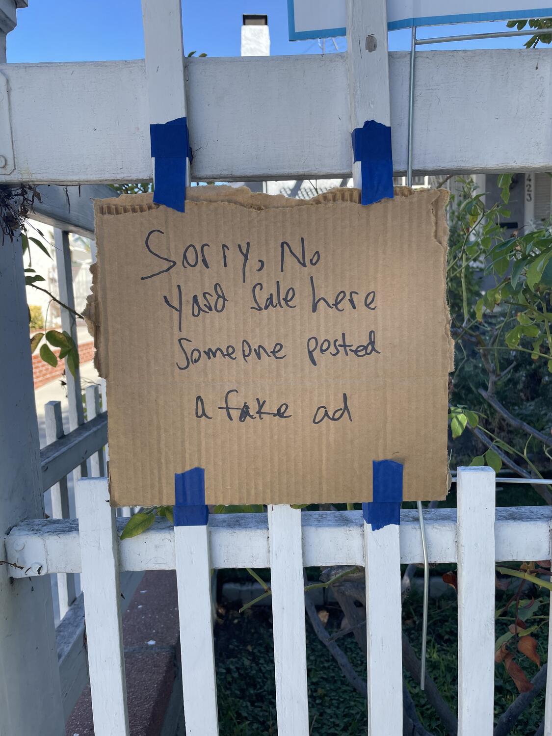 A cardboard sign taped to a fence. It reads â€œSorry, no yard sale here - someone posted a fake ad.â€�