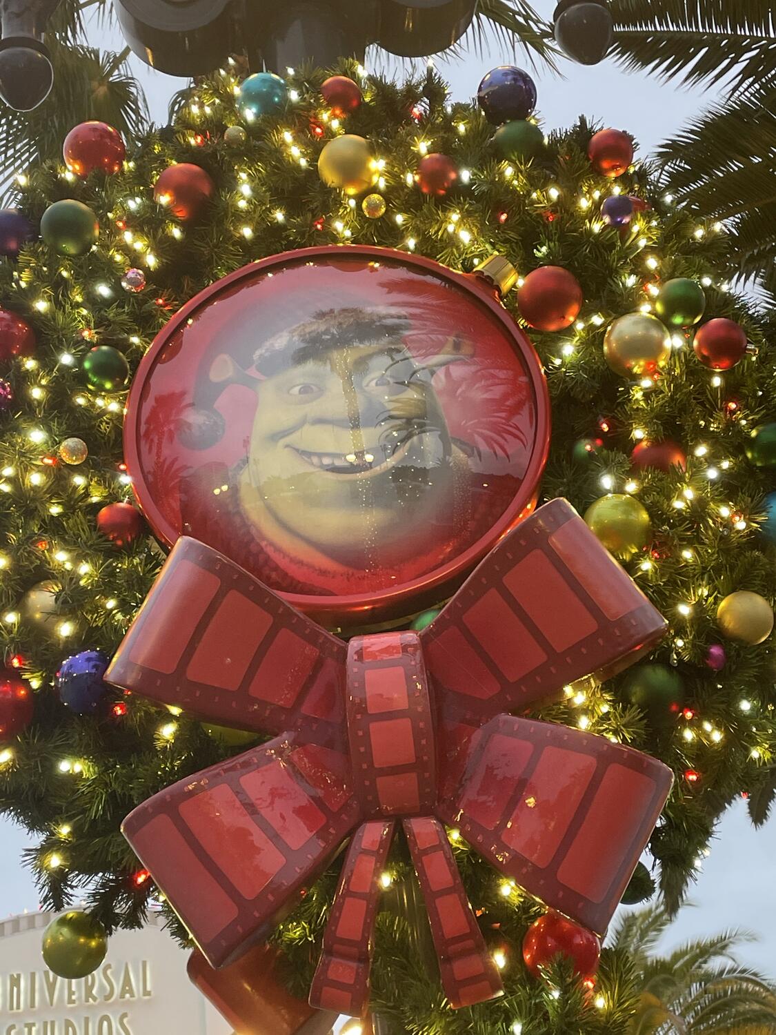 A Christmas wreath on a lamp post. In the center is a big ornament with Shrek's face inside.