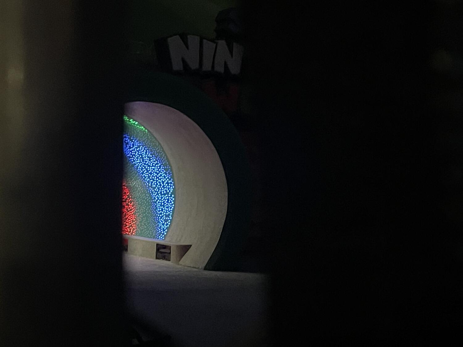 A peek at the entrance to Super Nintendo Land through a fence. The green warp pipe is lit up on the inside with colorful lights.
