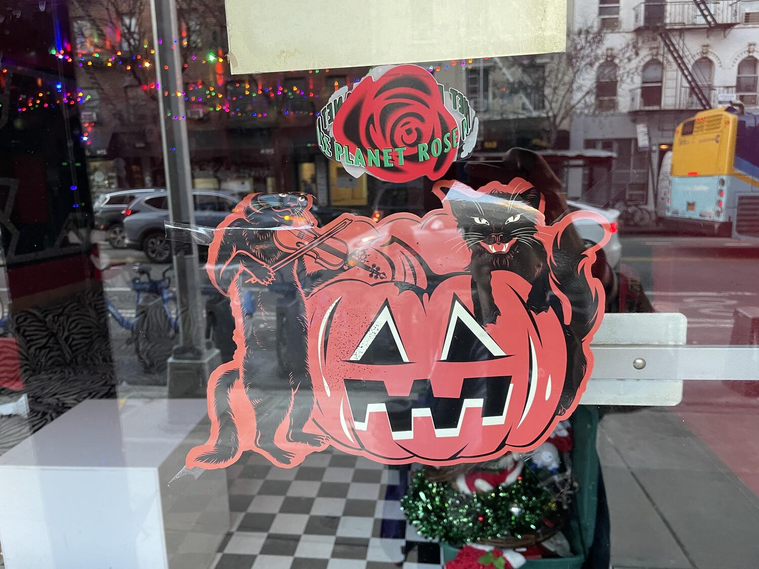 A vintage Halloween decoration depicting two black cats around a Jack-o-lantern, attached to the interior of a glass door