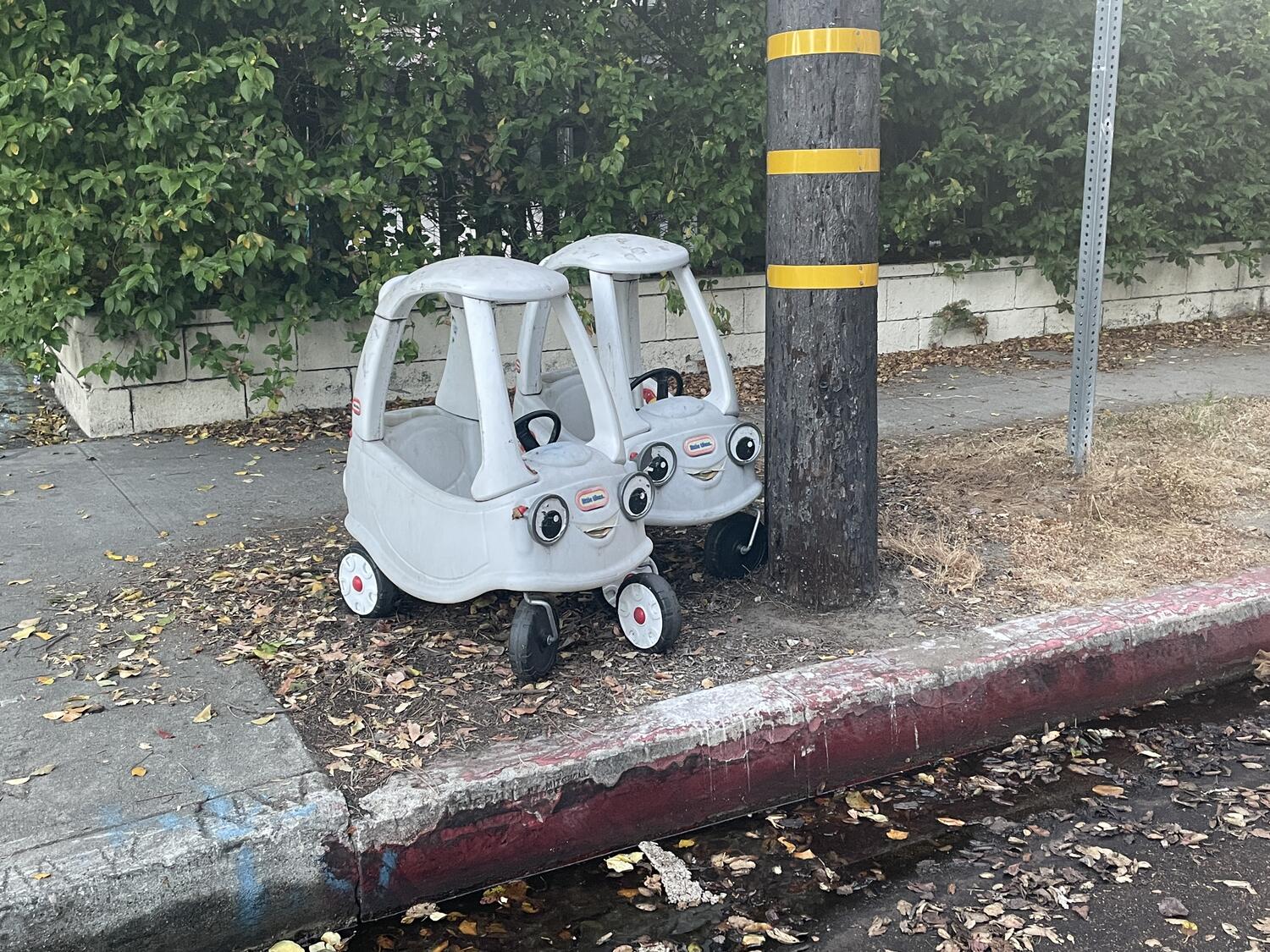 Two play cars sitting on a street corner. They are both eerily drained of color.