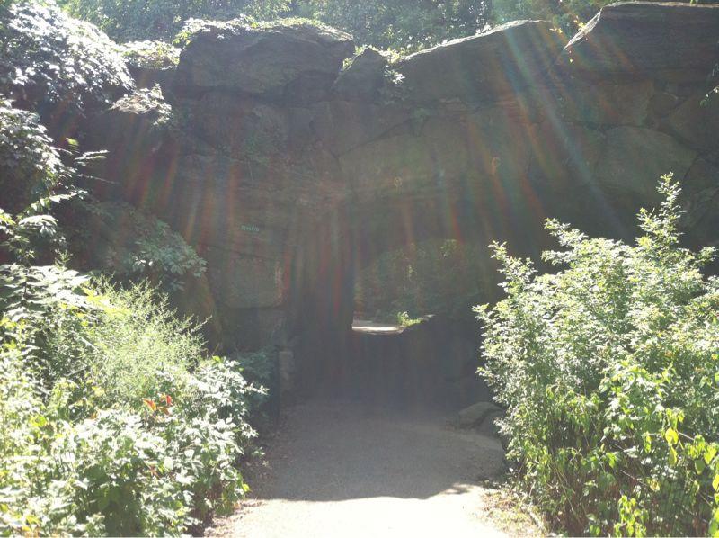 A gravel path leads through an arch carved into a tremendous stone outcropping toward more obscured greenery