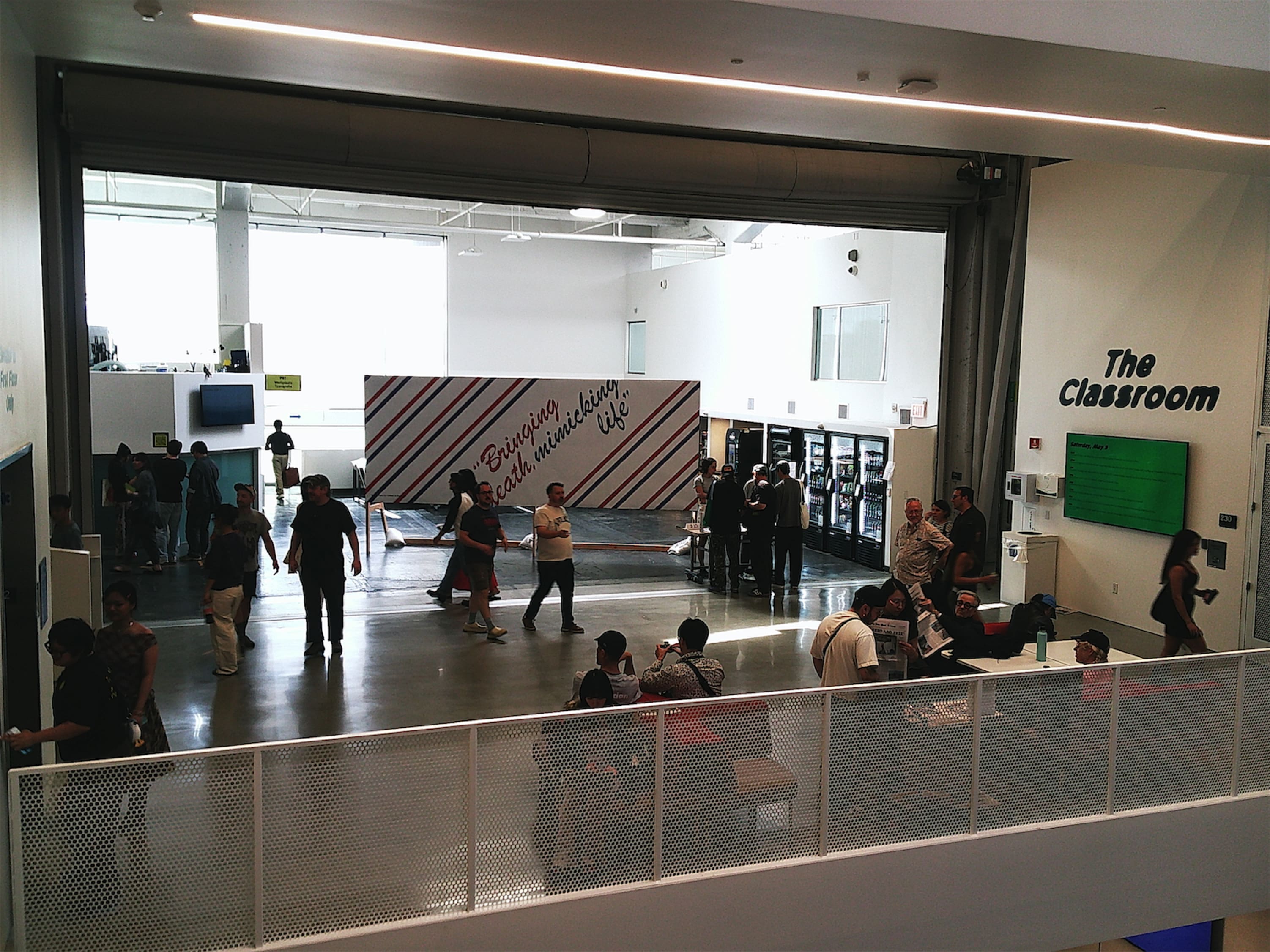 A distant shot of a glossy concrete floor. There's a big plywood billboard in the center of it that reads: Bringing death, mimicking life.
