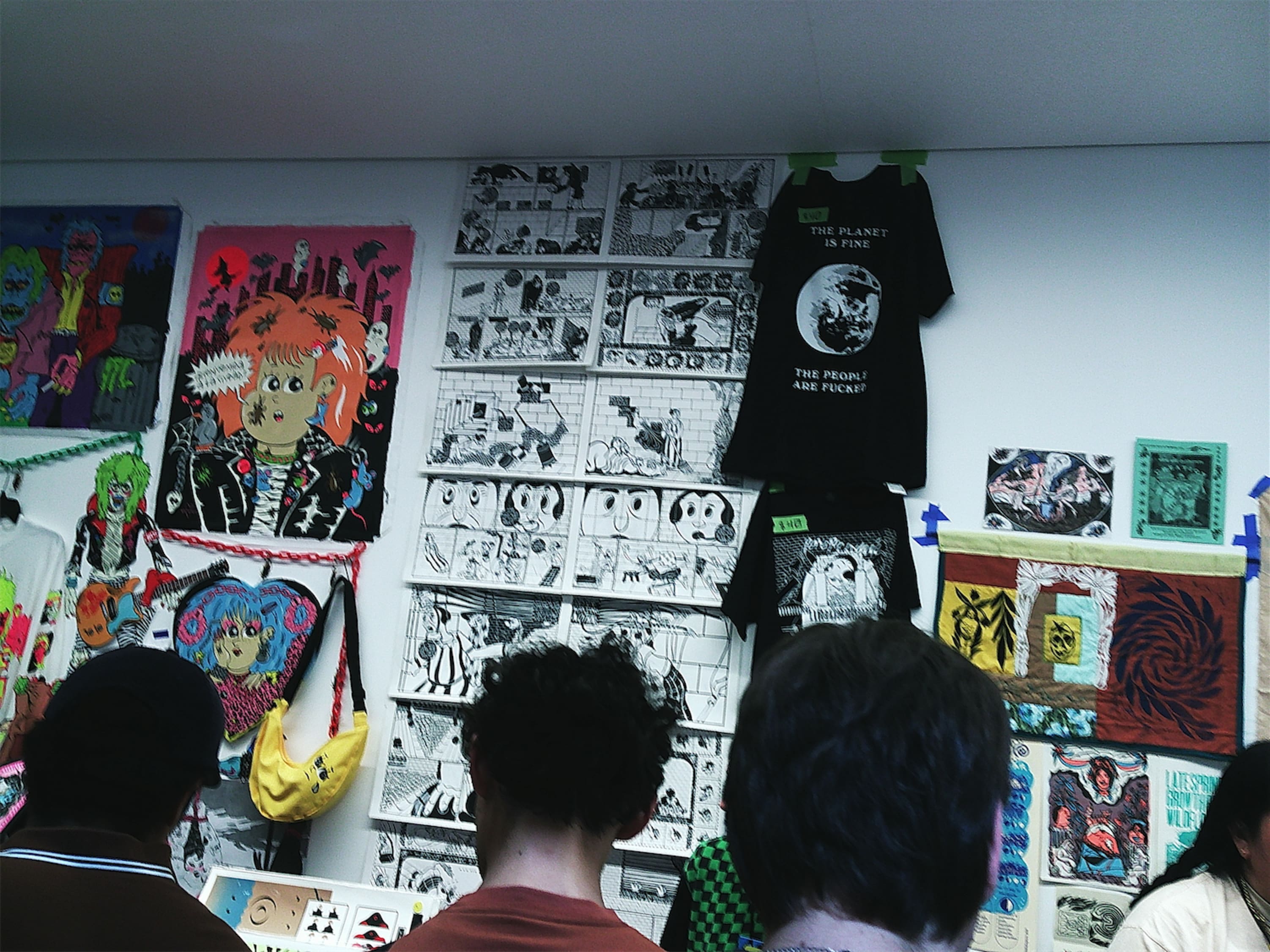 Prints pinned to a wall that all have a similar funny-pages aesthetic, bold black lines and characters with big dark eyes