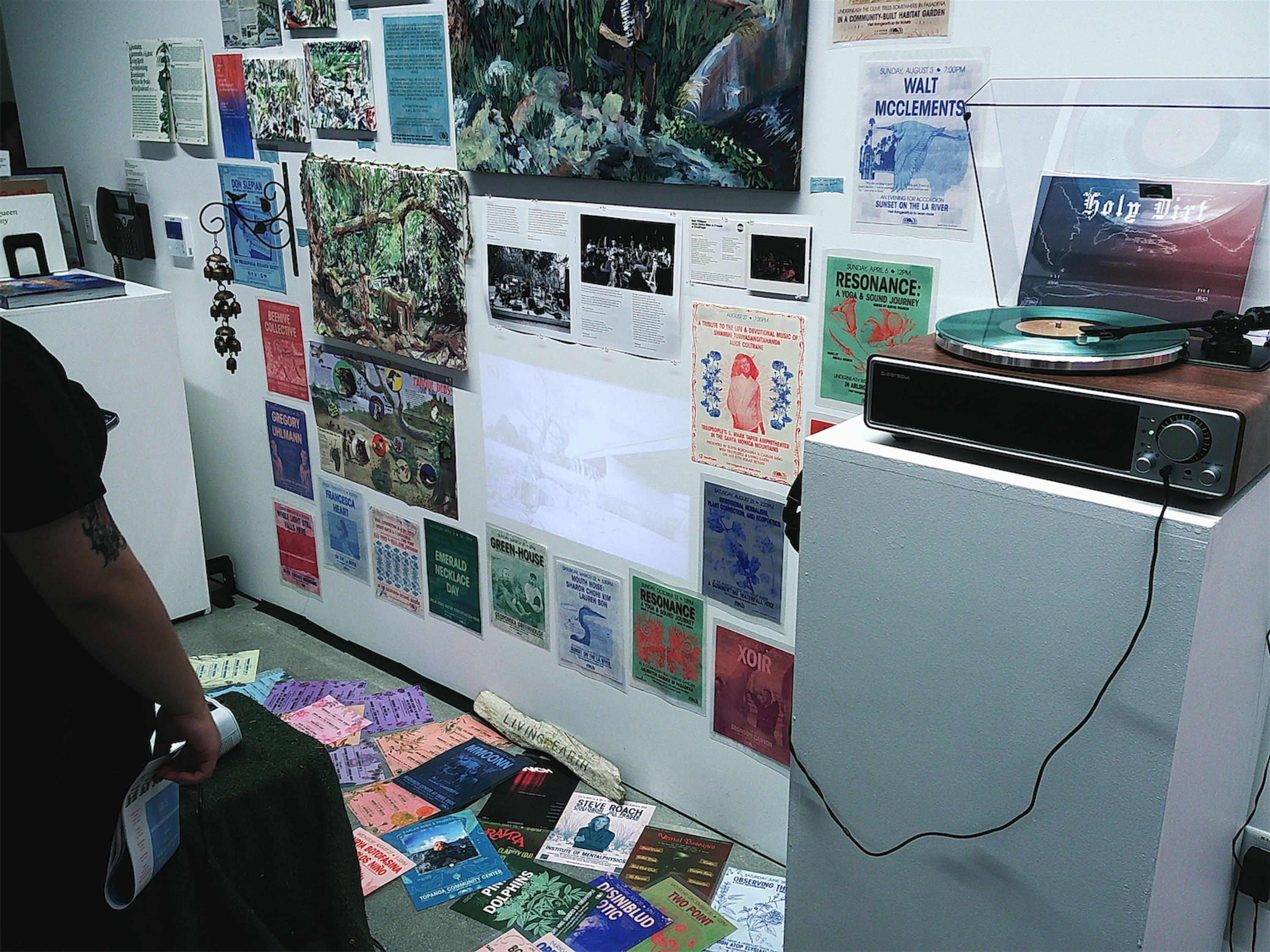 A busy installation of flyers and painted canvases from eye level down the floor and spilling out over it. Among the prints there is space for a modest projection.