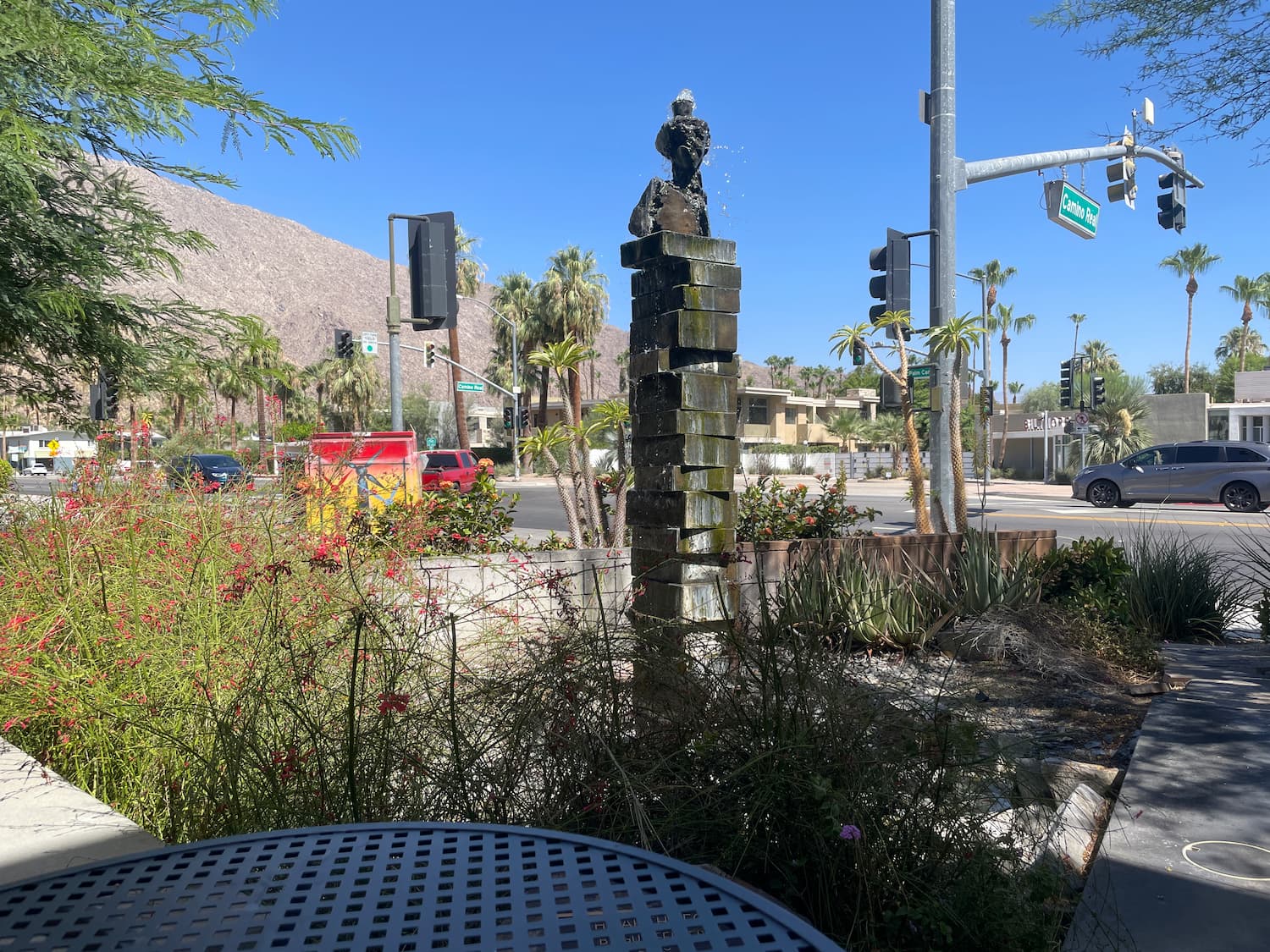 A fountain installed in a shady corner of an otherwise sun-blasted intersection, a modest mountain range in the distance and palm trees all around