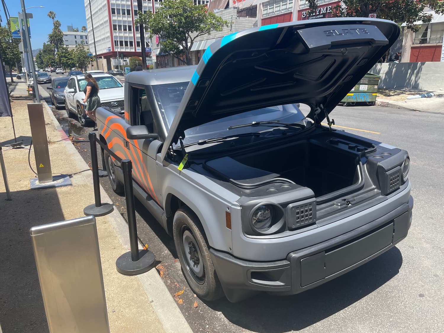 A pickup truck parked on the side of the road with crowd-control ropes around it. The hood is propped open, revealing a deep storage space, regrettably known as a "frunk" (front-trunk).