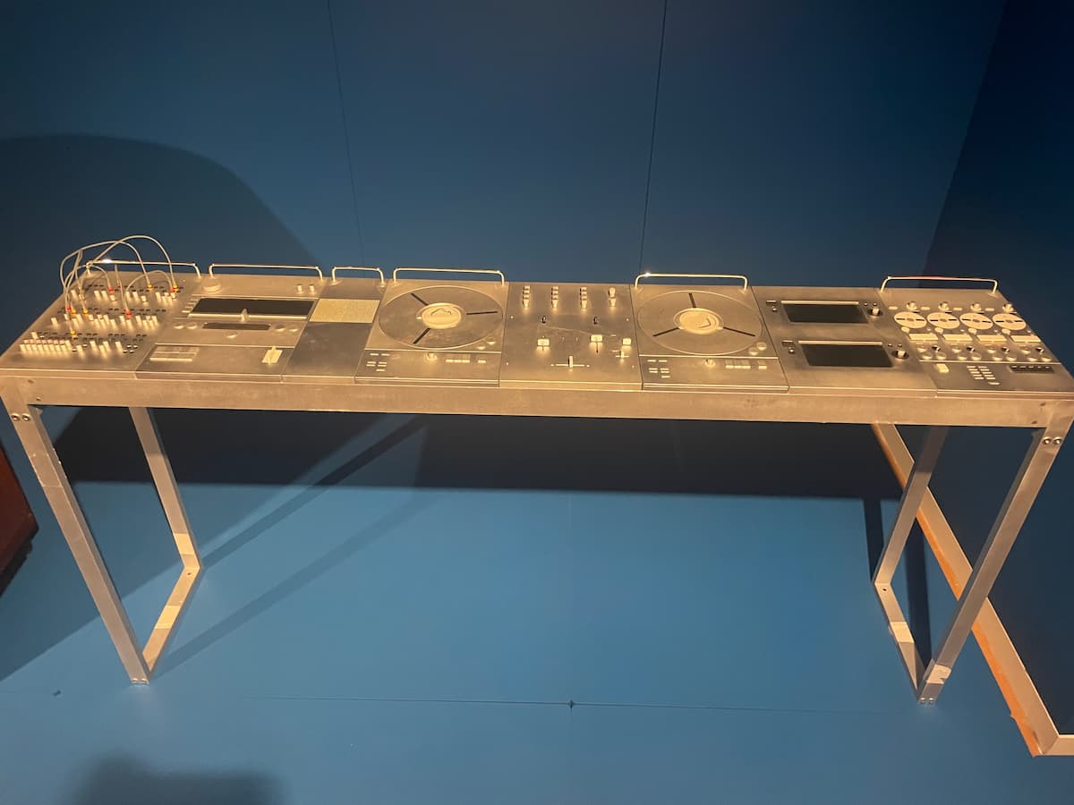 A long and shallow aluminum table on display. It's cover in rather inscrutable knobs, wires, screens, and buttons.