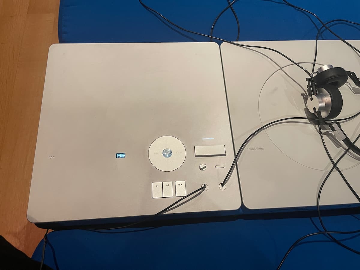 A large aluminum plate embedded in an upholstered bench. There's a tiny display, a few buttons, a circular jog wheel, and some headphone cables coming out of it.